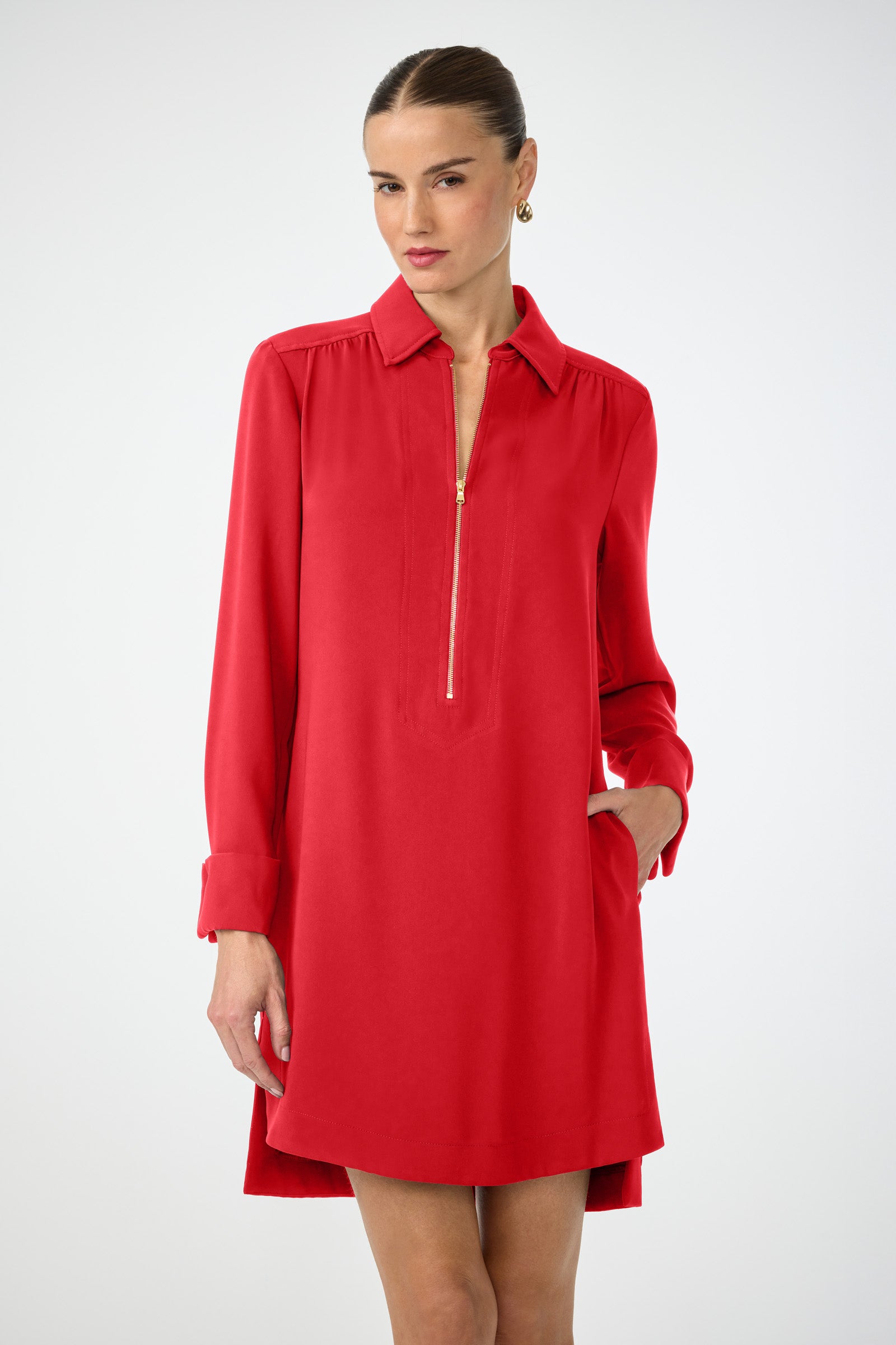 A woman poses confidently in the Darya Long-Sleeve Dress, featuring a front zipper and collar. She stands against a plain background with her hair tied back and one hand in her pocket.