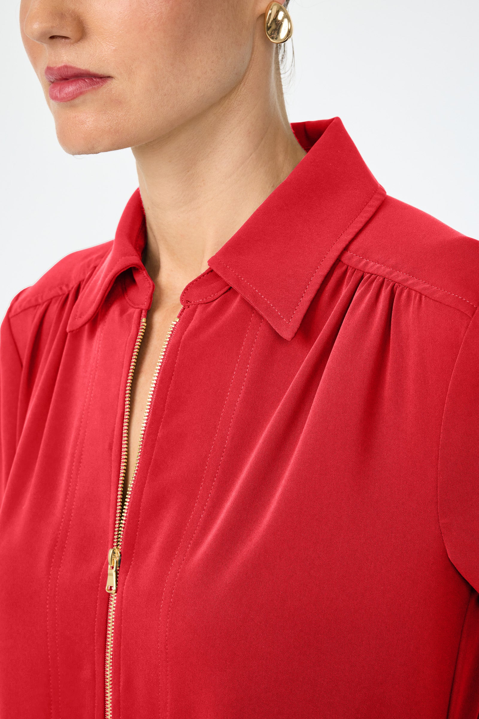 Close-up of a woman with light skin wearing the Darya Long-Sleeve Dress, featuring a red collared neckline and gold zipper. She pairs it with a gold hoop earring; only her lower face and upper torso are shown.