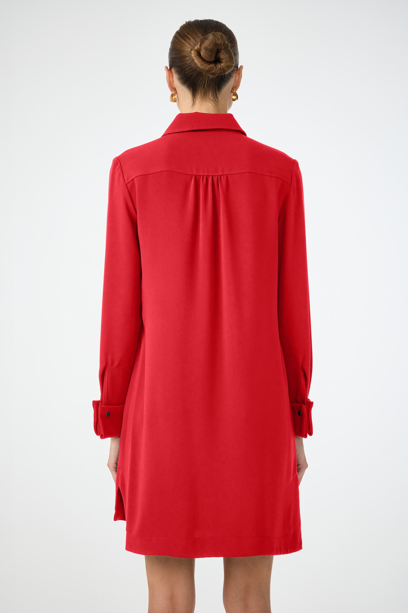 A woman with her hair in a neat bun is shown from the back wearing the Darya Long-Sleeve Dress, a knee-length red style, against a plain white background.