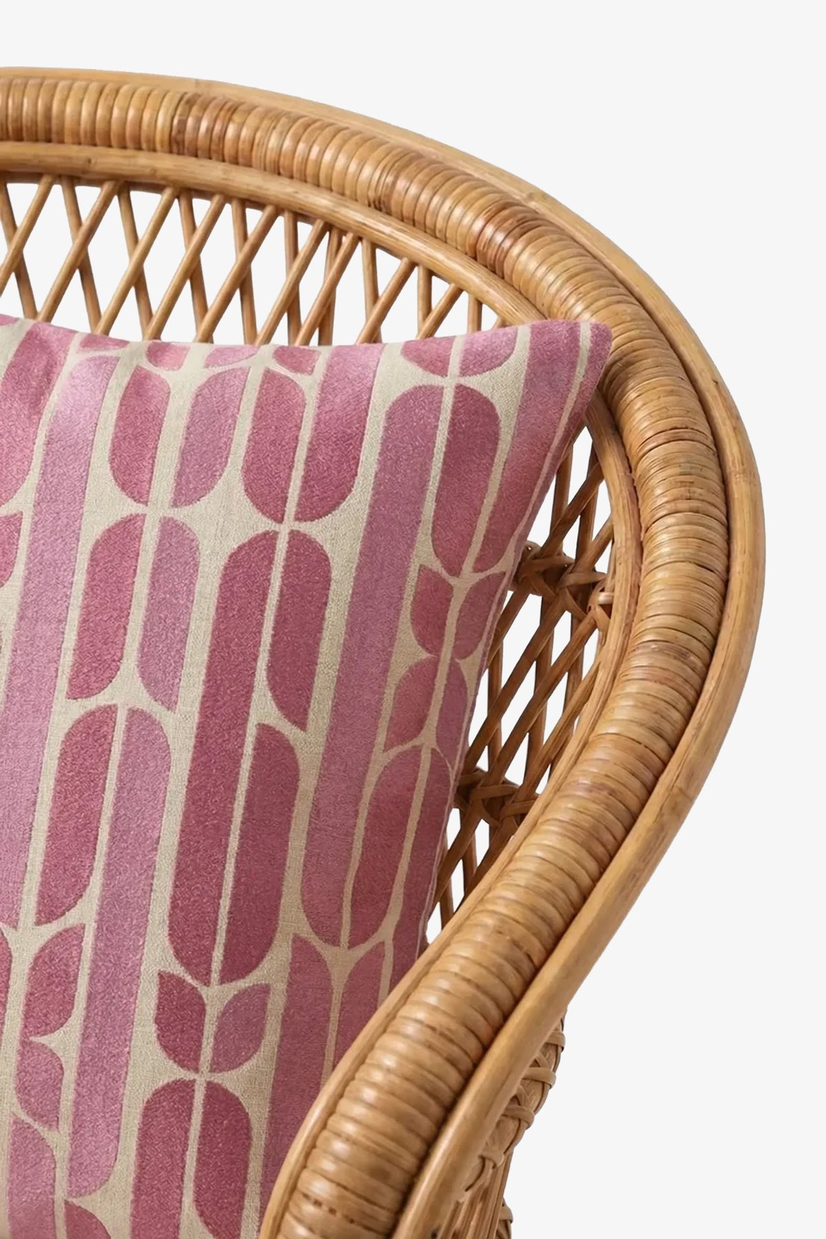 A close-up of the Palmdale Embroidered Square Pillow, featuring ombré pink and beige geometric patterns with curved and vertical shapes on a wicker chair, set against a plain white background.