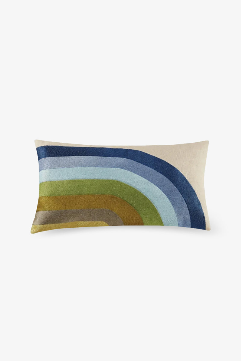 The Calistoga Embroidered Lumbar Pillow features a cream background with curved blue, green, and mustard yellow stripes in a partial rainbow design and colorful embroidery.