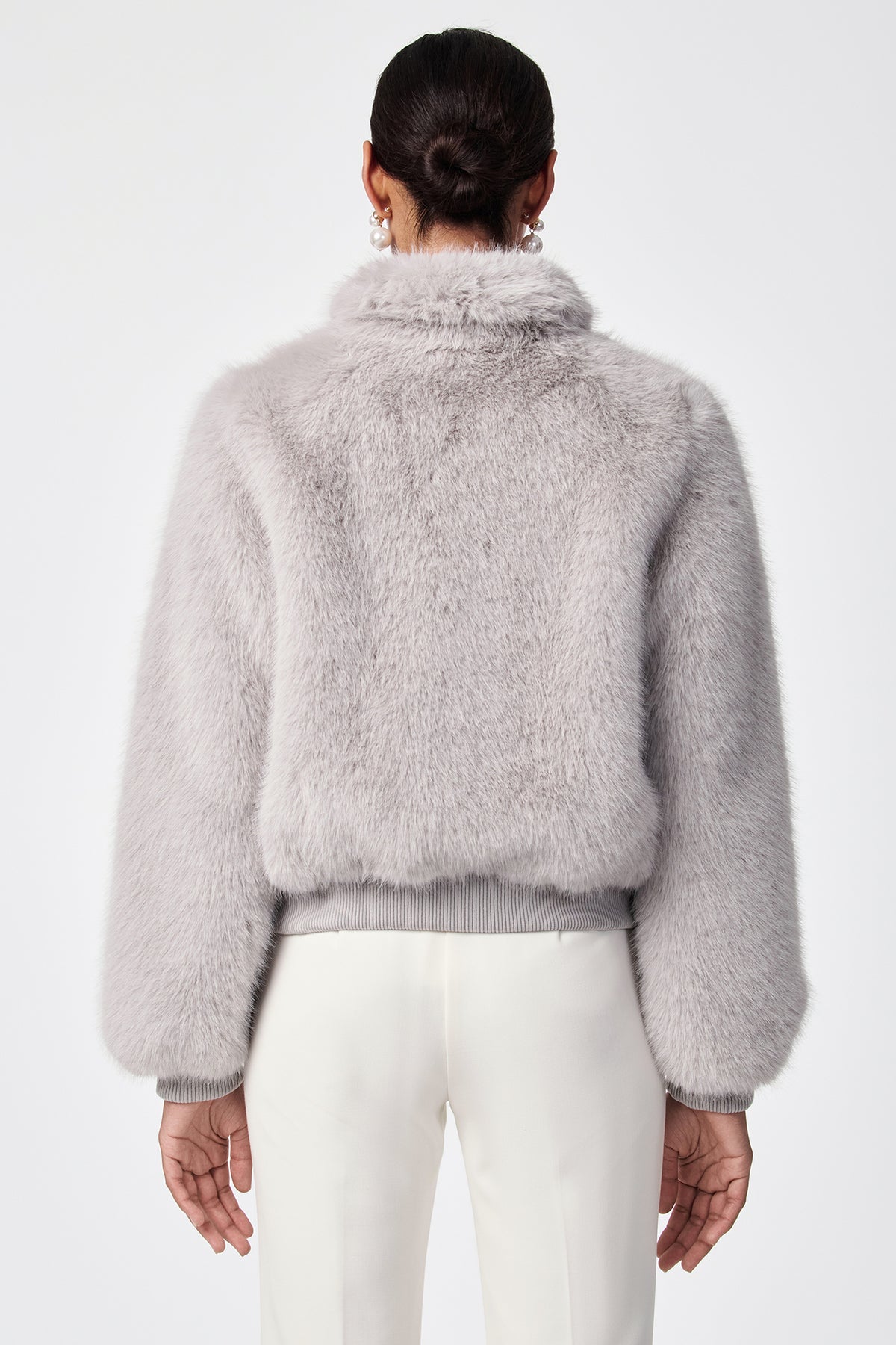 A person with dark hair in a low bun is shown from the back, wearing the Morris Short Faux Fur Coat in light gray and white pants against a plain white background.