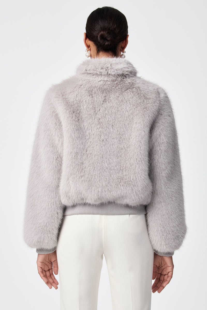 A person with dark hair in a low bun is shown from the back, wearing the Morris Short Faux Fur Coat in light gray and white pants against a plain white background.