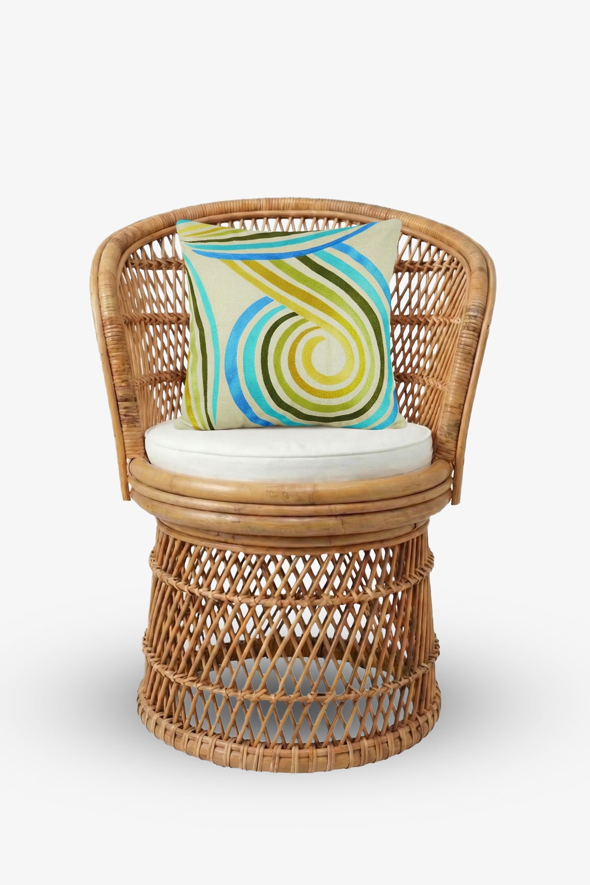 A round wicker chair with a beige seat cushion is styled with the Calexico Embroidered Square Pillow—measuring 20″x20″ and showcasing blue, green, and yellow swirled embroidery on a soft down-filled cover—set against a plain white background.