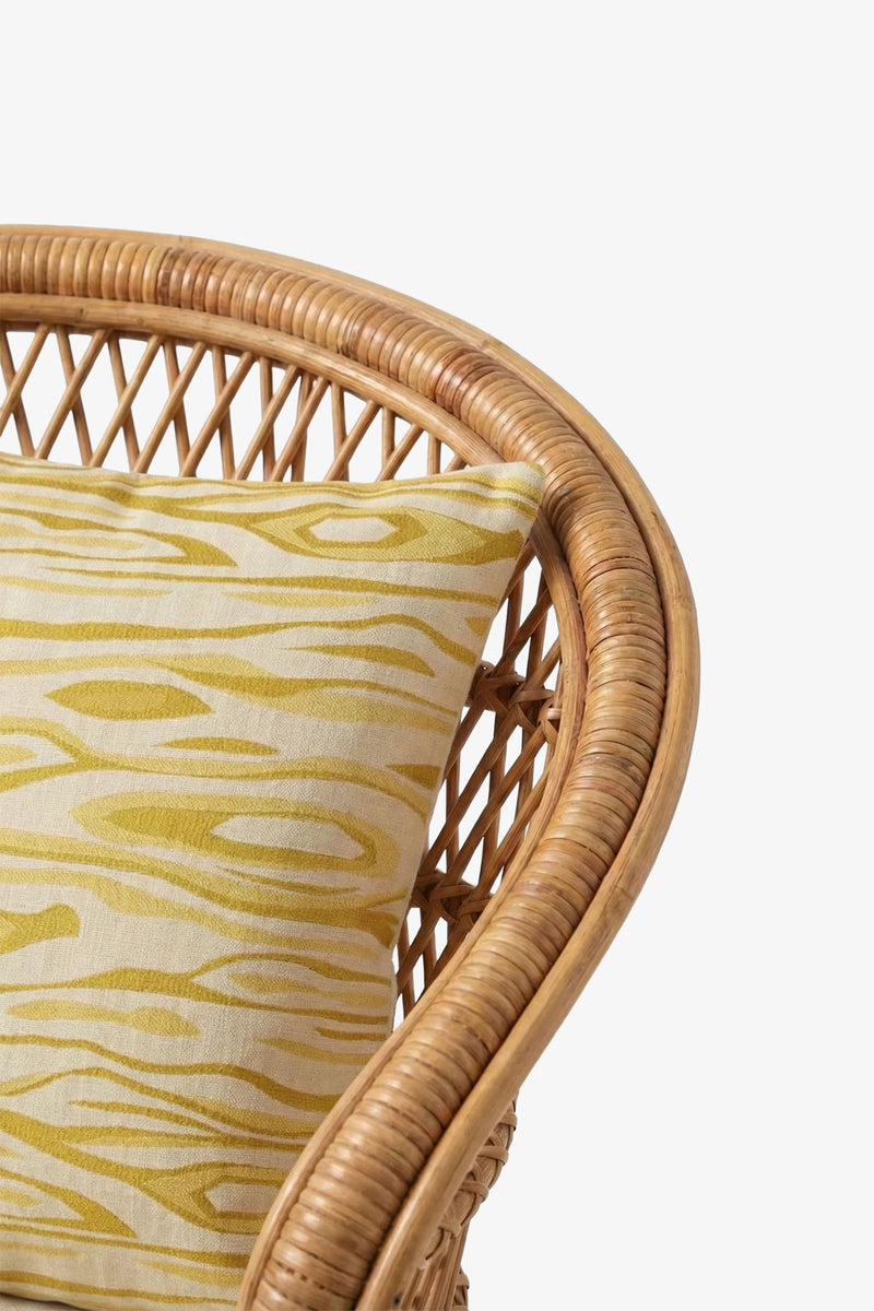 Curved rattan chair with the Monterey Embroidered Square Pillow, showcasing a yellow and white pattern and wood grain-inspired design, displayed against a plain white background.