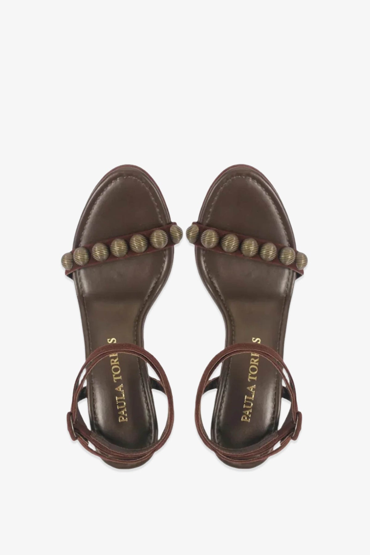Introducing the Paula Torres Espanha Sandal: a brown open-toe design featuring a beaded strap across the toes and elegant ankle straps. The sandals are enhanced with an architectural triangle heel and a cushioned insole stamped with PAULA TORRES in gold, offering a perfect balance of style and comfort.
