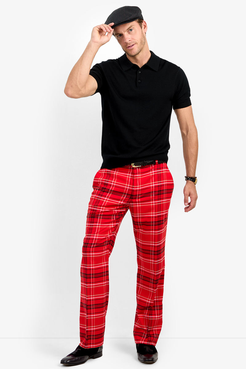A man wearing a black polo shirt, Dirk Trouser in classic fit red plaid, black shoes, and a gray cap poses against a plain white background, holding the brim of his cap with one hand.