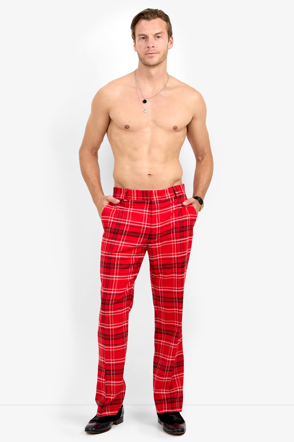 A shirtless man stands with hands in pockets, modeling Dirk Trouser in red plaid and black shoes against a plain white background.