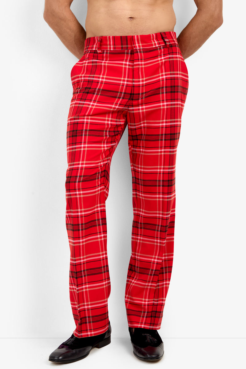A person models the Dirk Trouser in classic fit red plaid, standing with hands in pockets, black shoes on, upper body bare against a plain white background.