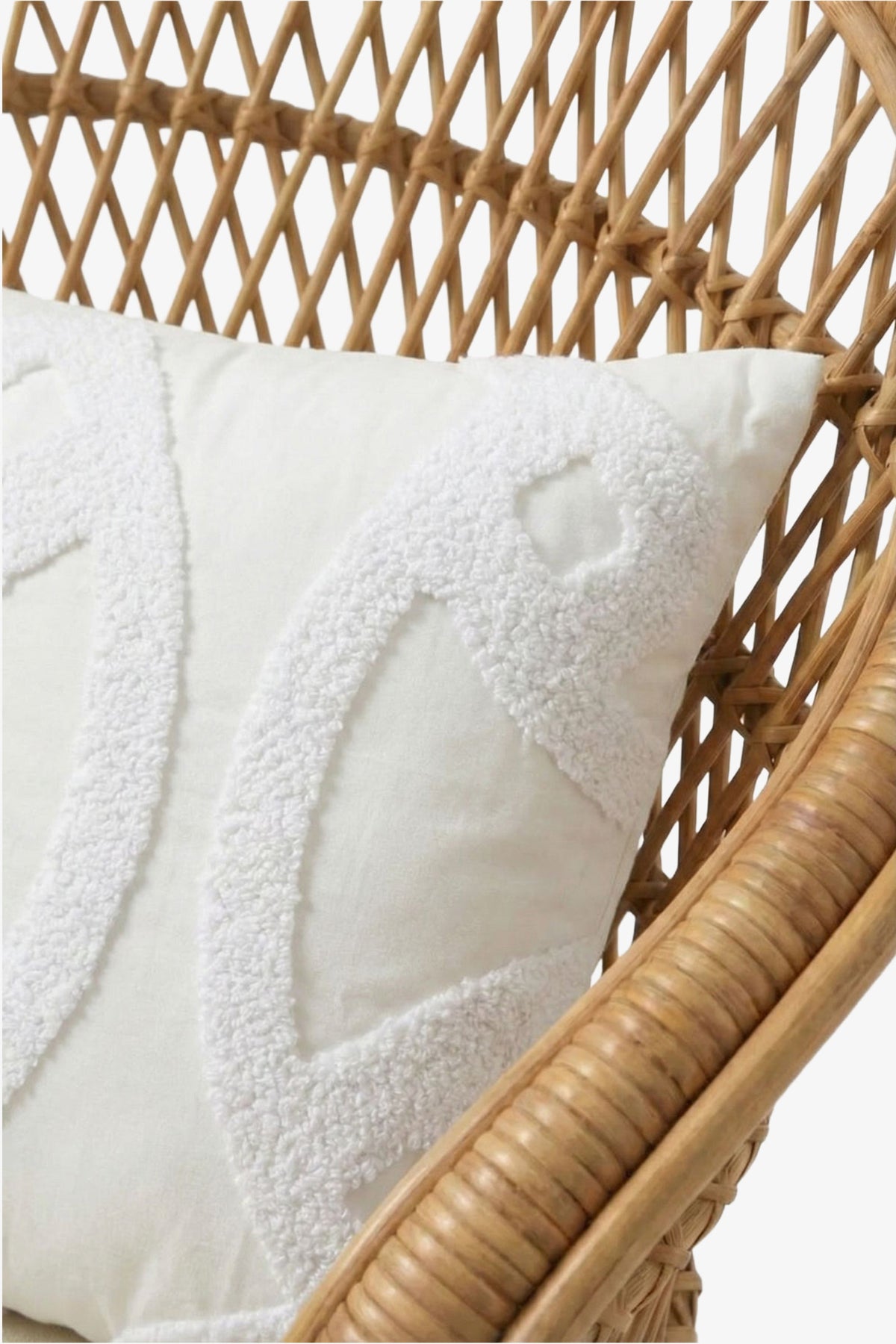 A close-up of the Santorini Embroidered Lumbar Pillow, showcasing its white tufted geometric pattern, placed on a woven rattan chair against a white background.
