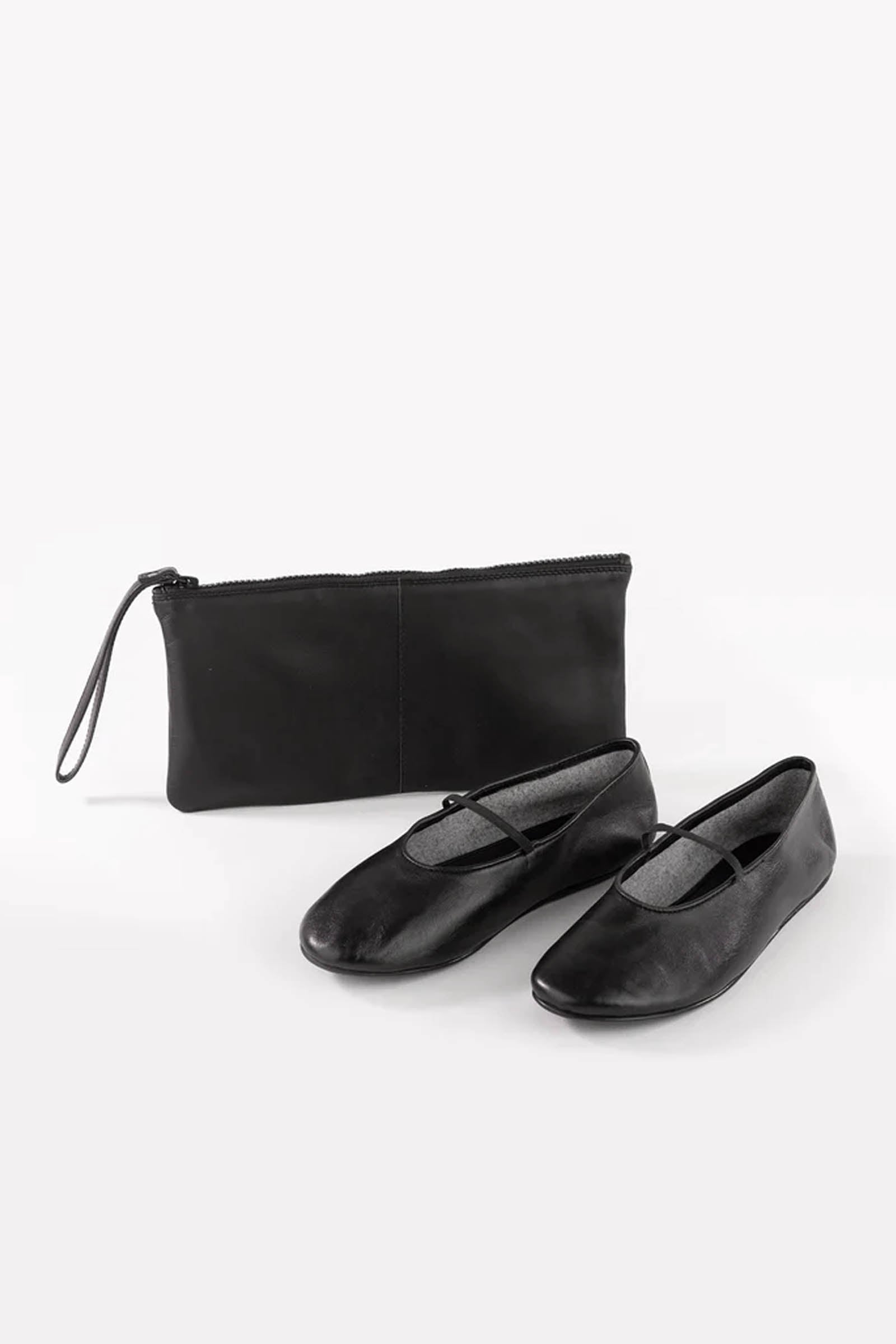 The Seychelles Neon Moon Travel Duo features a pair of simple black ballet flats with a leather upper and thin straps, displayed alongside a matching black zippered pouch on a white background.