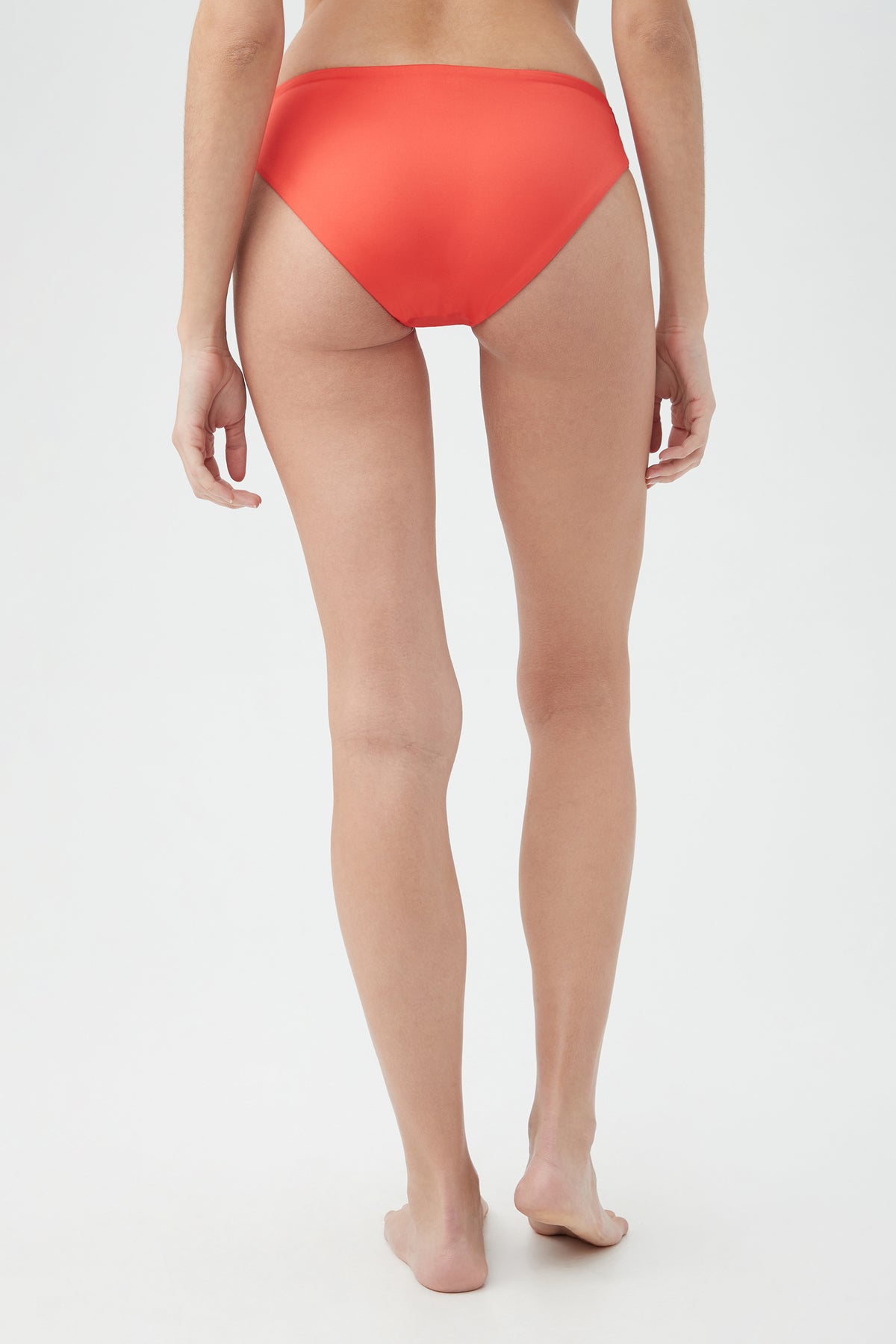 A person stands barefoot on a white background, shown from behind, wearing the Women's Monaco Shirred Hipster Swim Bottom in bright red.