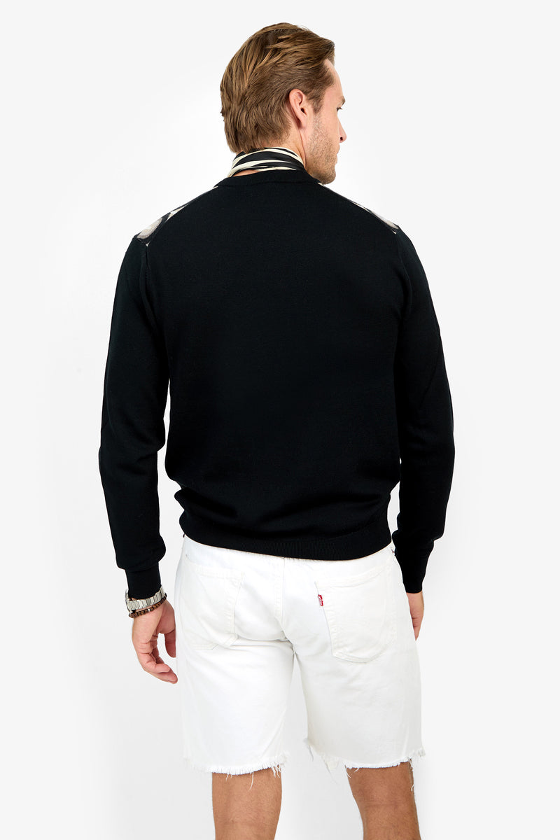 A man with light brown hair, wearing a black jacket with striped collar, white frayed shorts, and the Chrysler Sweater, stands with his back to the camera against a plain white background.