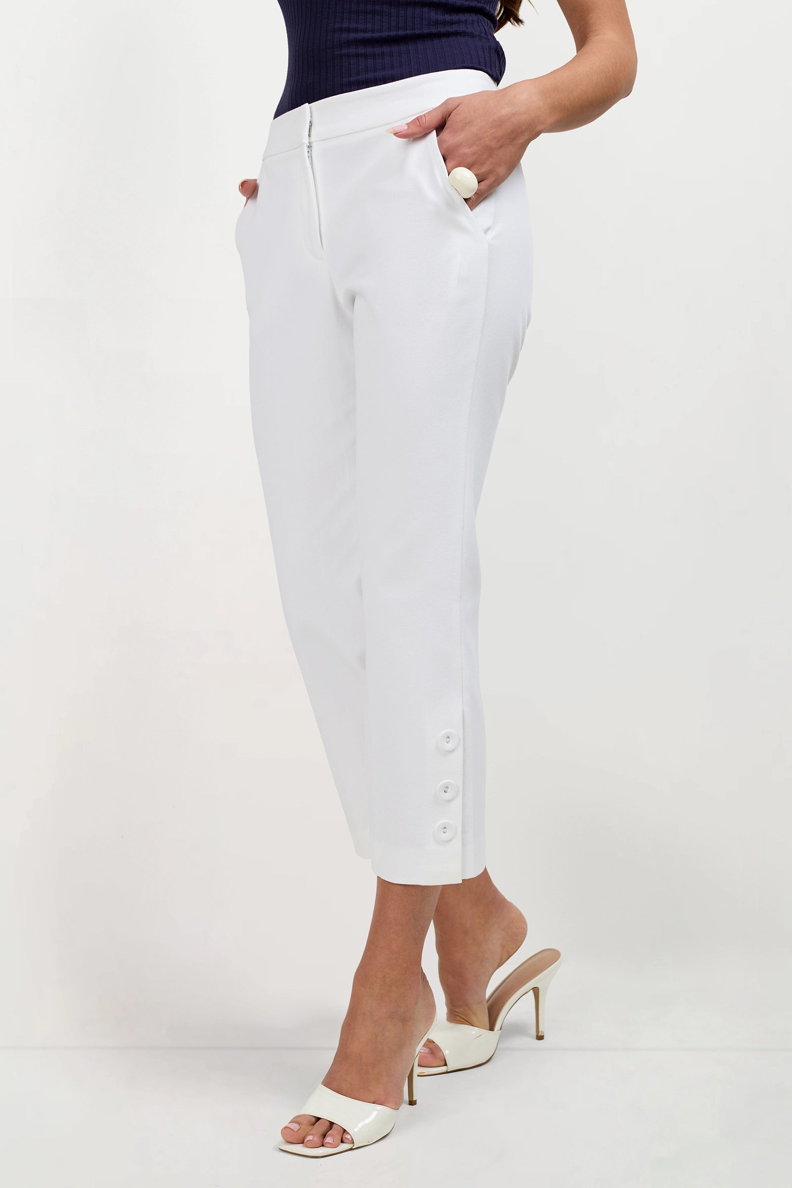 A person wearing Ore Button-Hem Cropped Pants styled with ivory open-toe heeled sandals and a dark sleeveless top, standing against a plain white background.