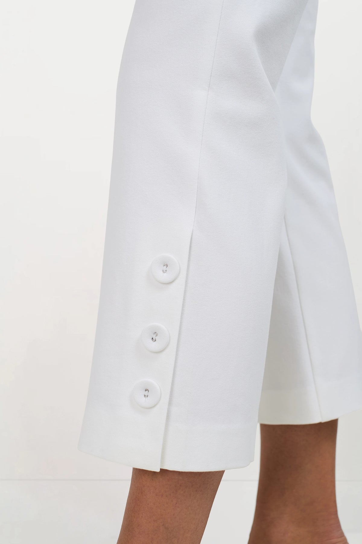 Cropped view of a person wearing Ore Button-Hem Cropped Pants, featuring three large white buttons on the side near the hem, against a plain light background.