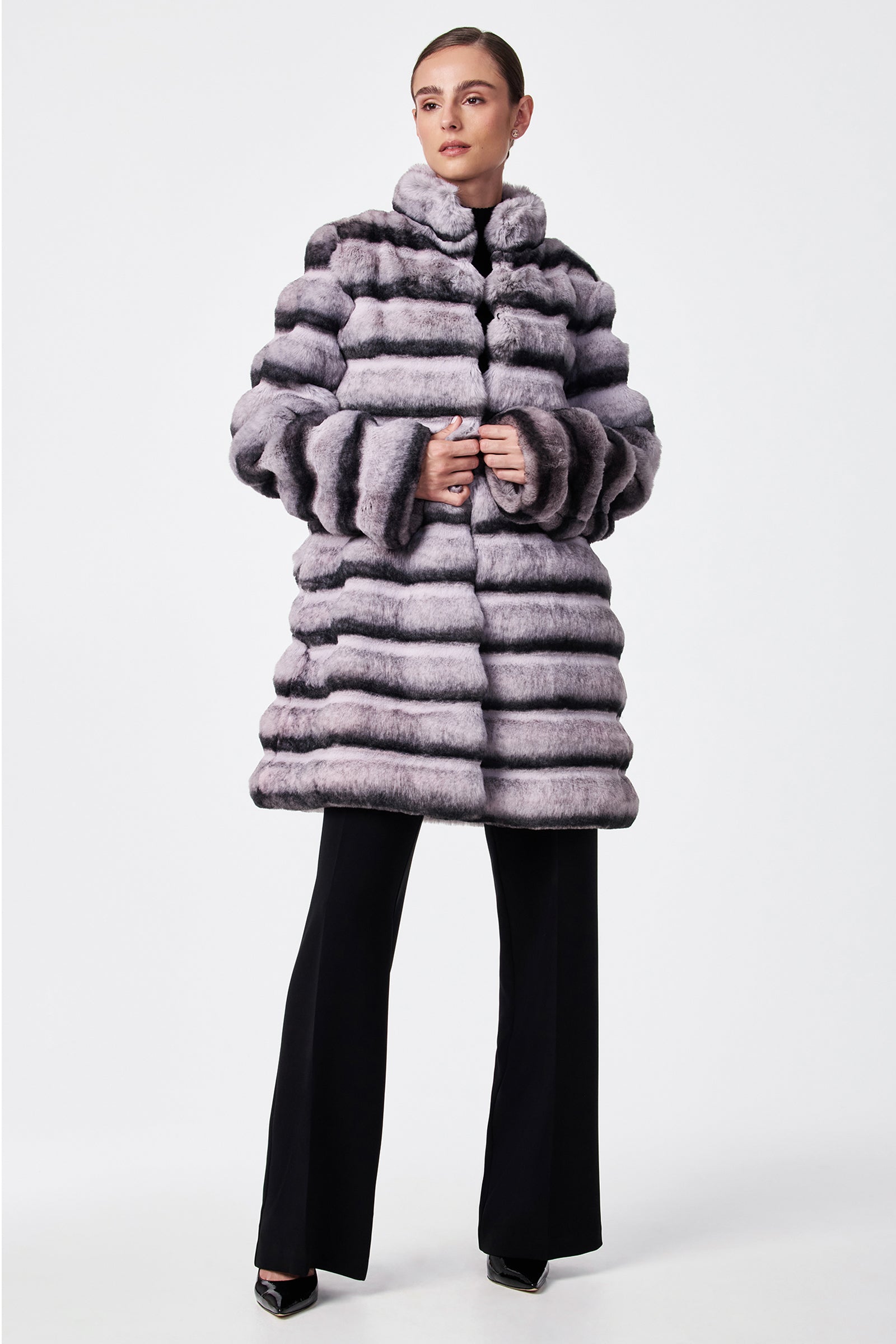 A woman wears the Mikel 2 Faux Fur Mid-Length Coat with black wide-leg pants and black shoes, standing against a plain white background.