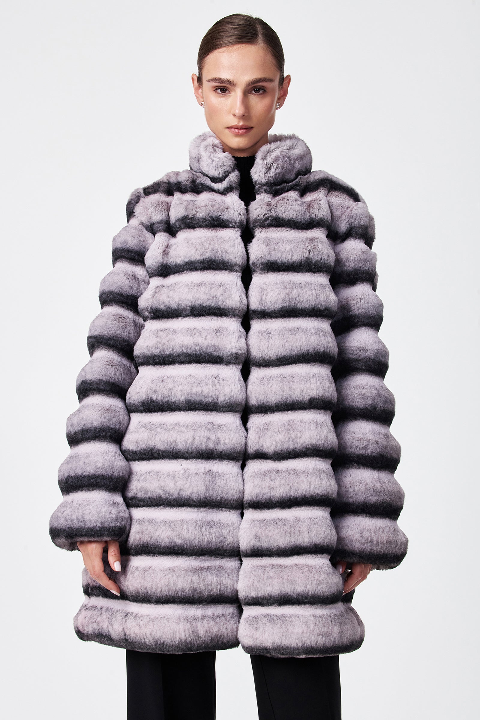 A person models the Mikel 2 Faux Fur Mid-Length Coat, featuring thick, striped light gray and black faux fur with a high collar and puffy horizontal quilted design, standing against a plain white background.