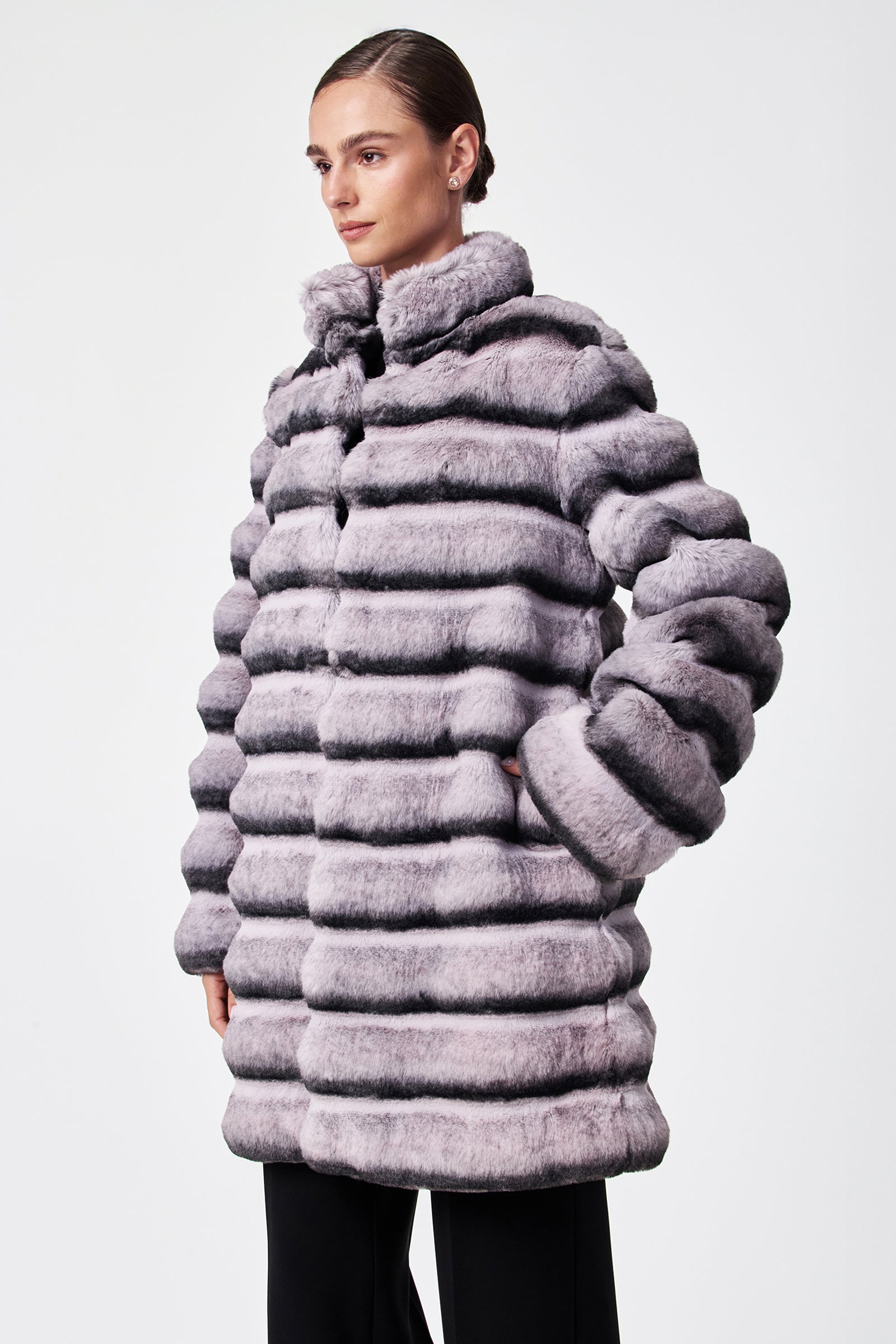 A person models the Mikel 2 Faux Fur Mid-Length Coat, featuring thick light purple and gray stripes and a high collar, against a plain white background.