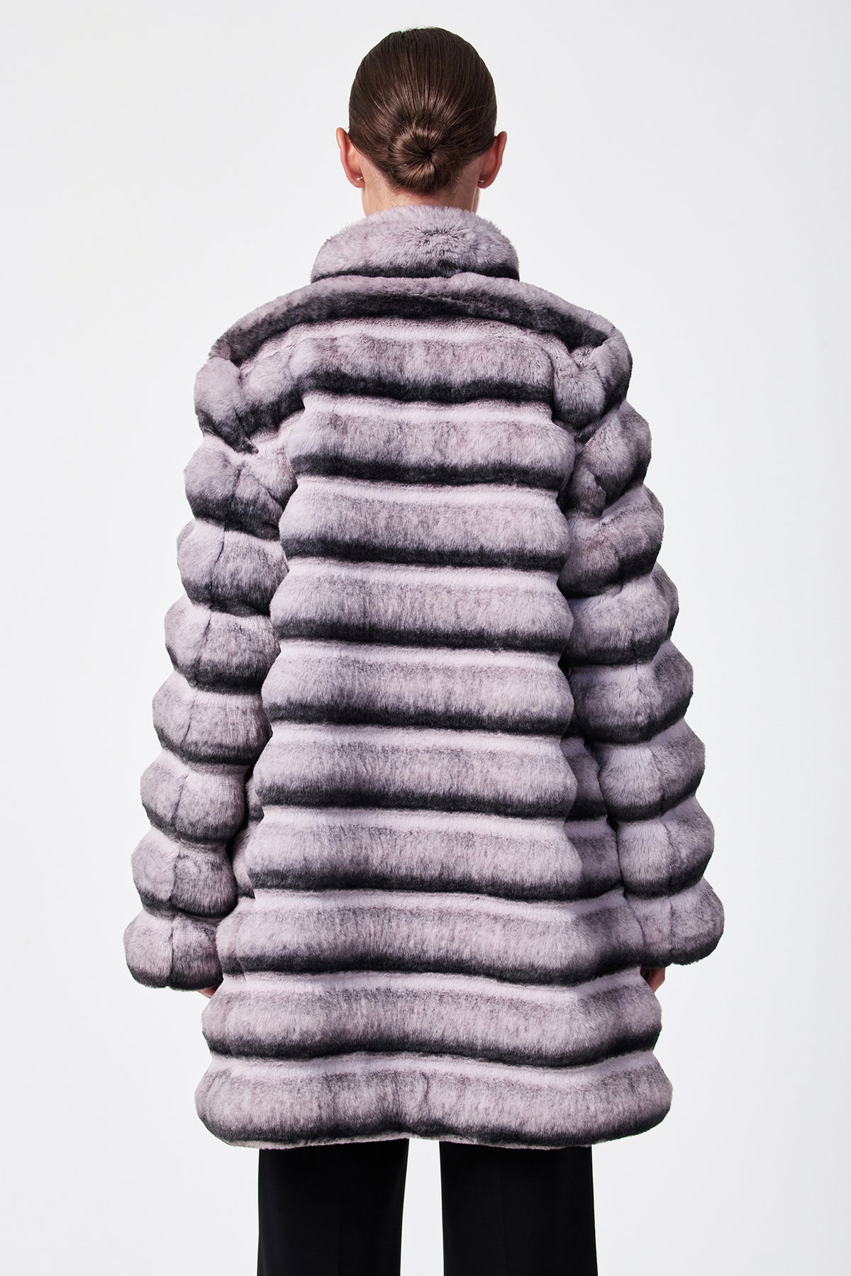 Seen from behind against a plain white background, a person with hair in a neat bun wears the Mikel 2 Faux Fur Mid-Length Coat, featuring thick horizontal stripes in light and dark gray with a high collar.