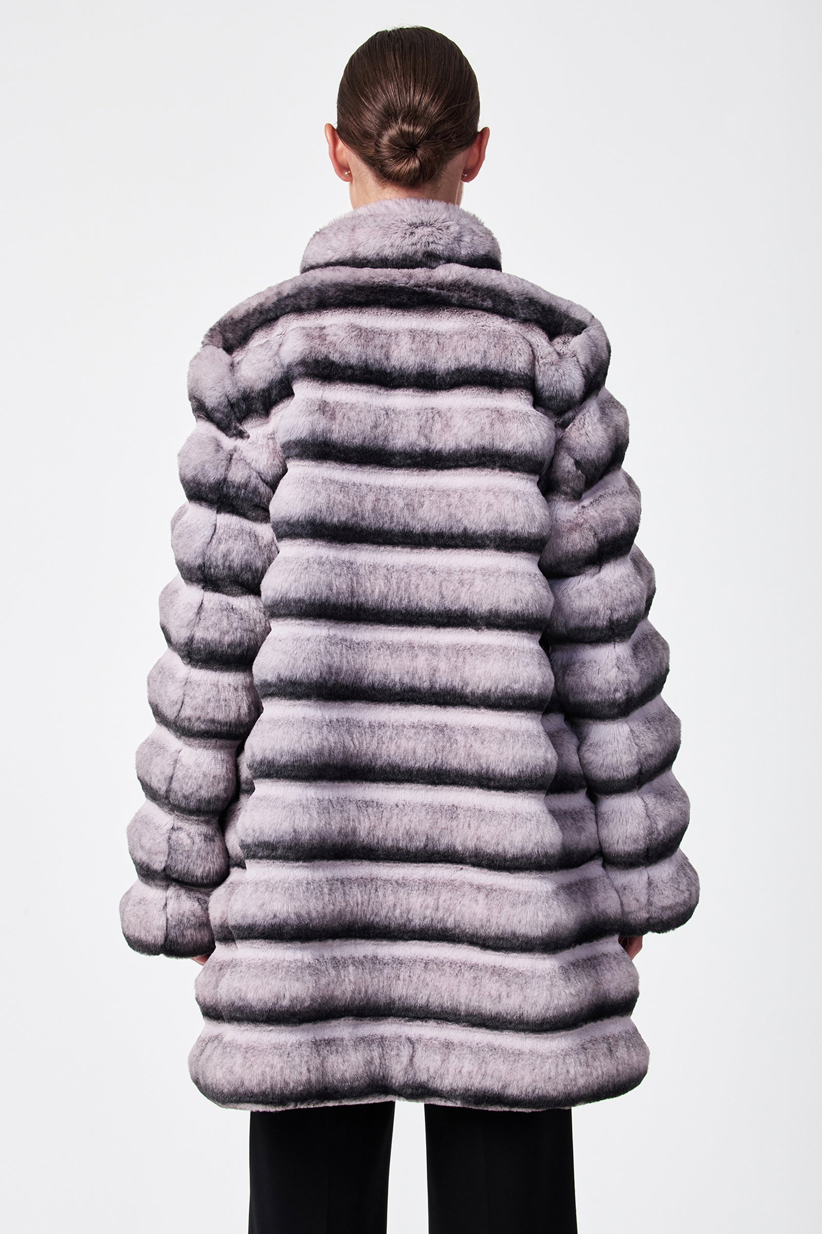 Seen from behind against a plain white background, a person with hair in a neat bun wears the Mikel 2 Faux Fur Mid-Length Coat, featuring thick horizontal stripes in light and dark gray with a high collar.