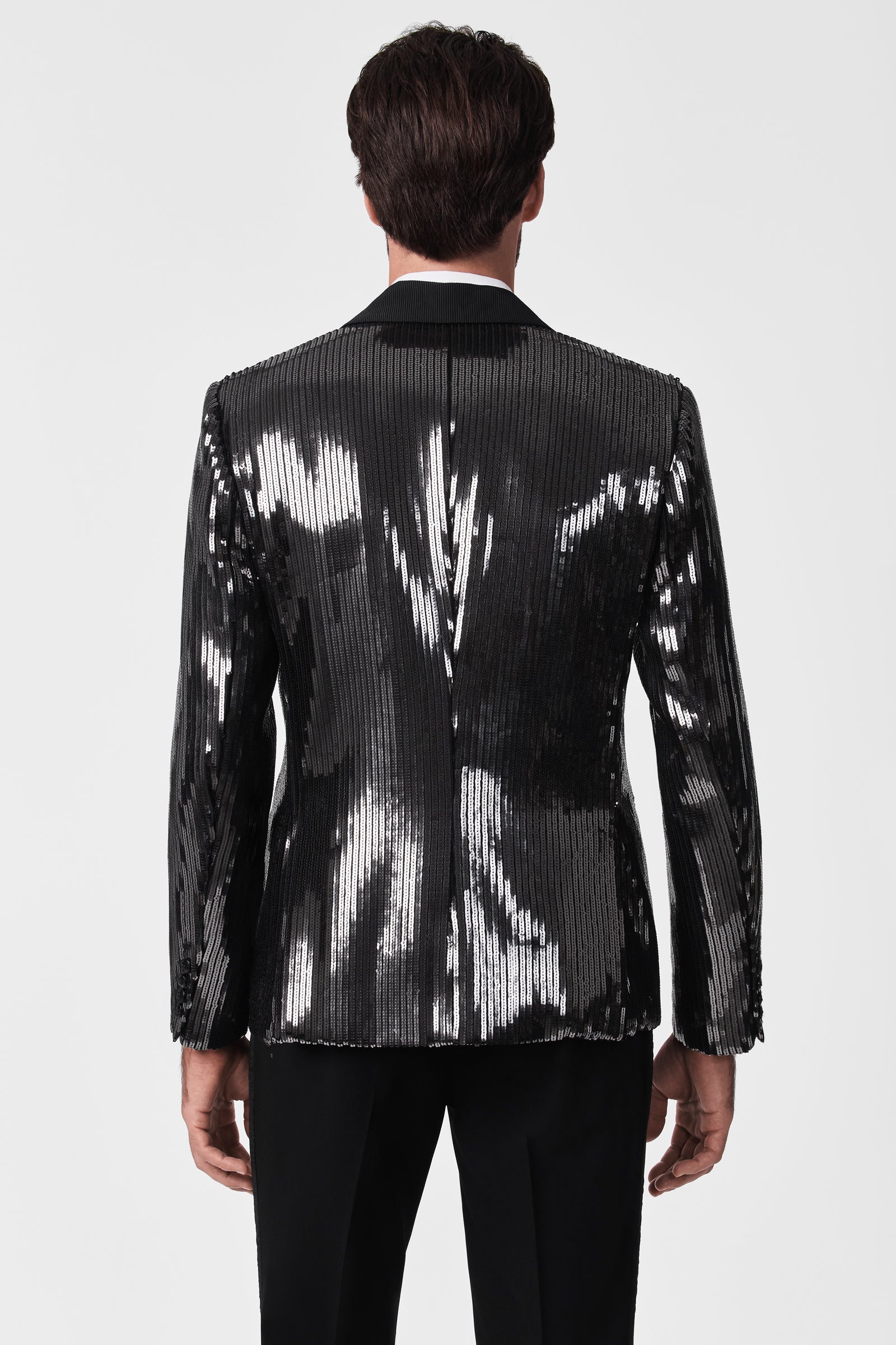 A man is seen from behind wearing the Coleman Blazer—a shiny black sequined piece with vertical lines—paired with black dress pants, set against a plain white background.