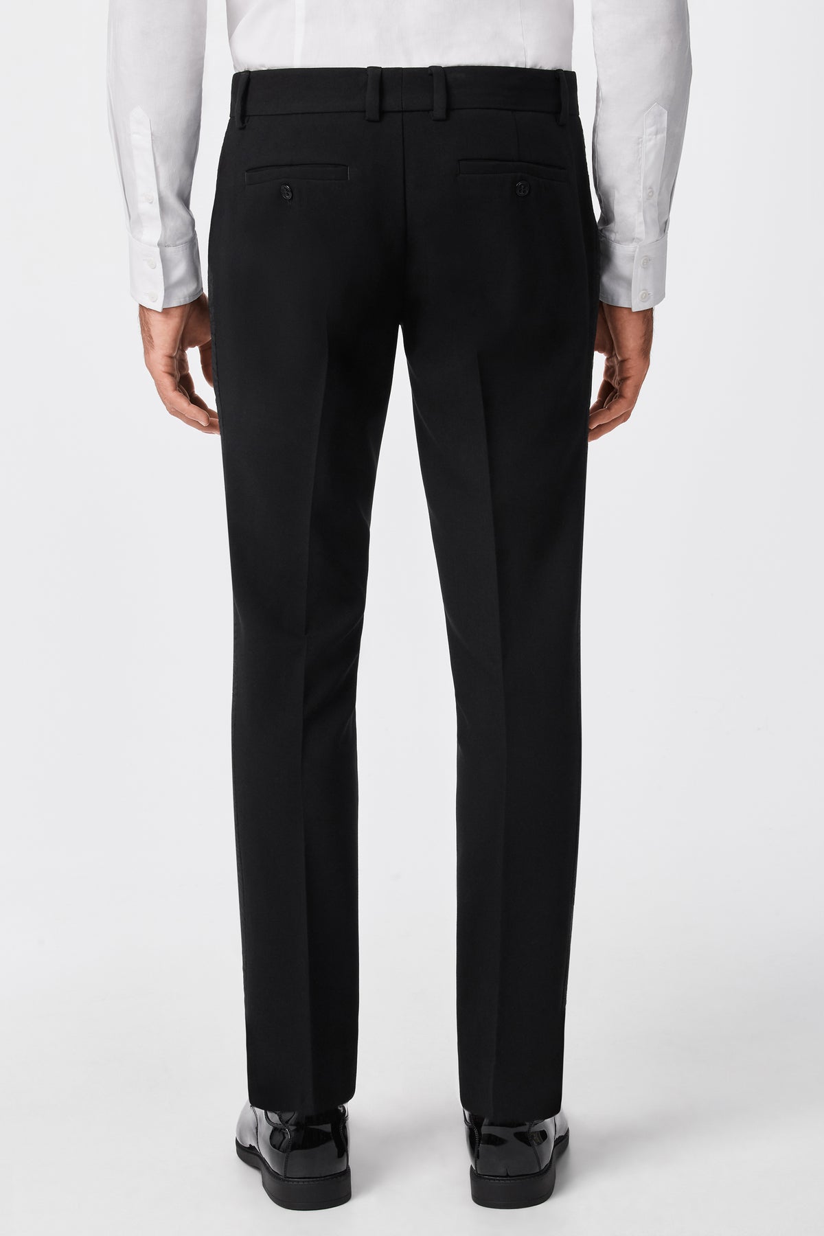A person is shown from the back wearing the Adrian Tux Trouser, featuring belt loops and buttoned back pockets, paired with a white dress shirt against a plain white background.