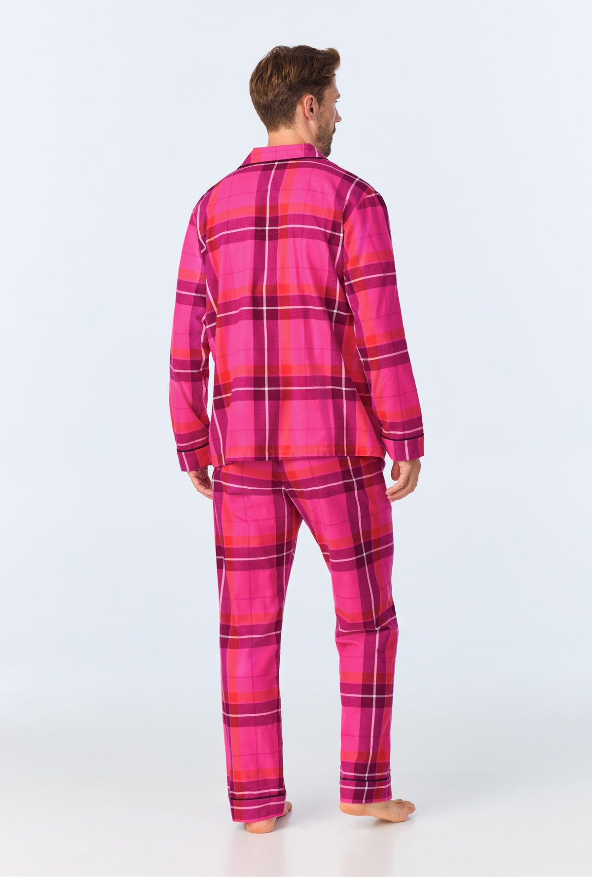 A man stands barefoot, back to the camera, wearing the Aurora Plaid Mens Long Sleeve Long Pant Flannel PJ Set in bright pink and purple against a plain light background.