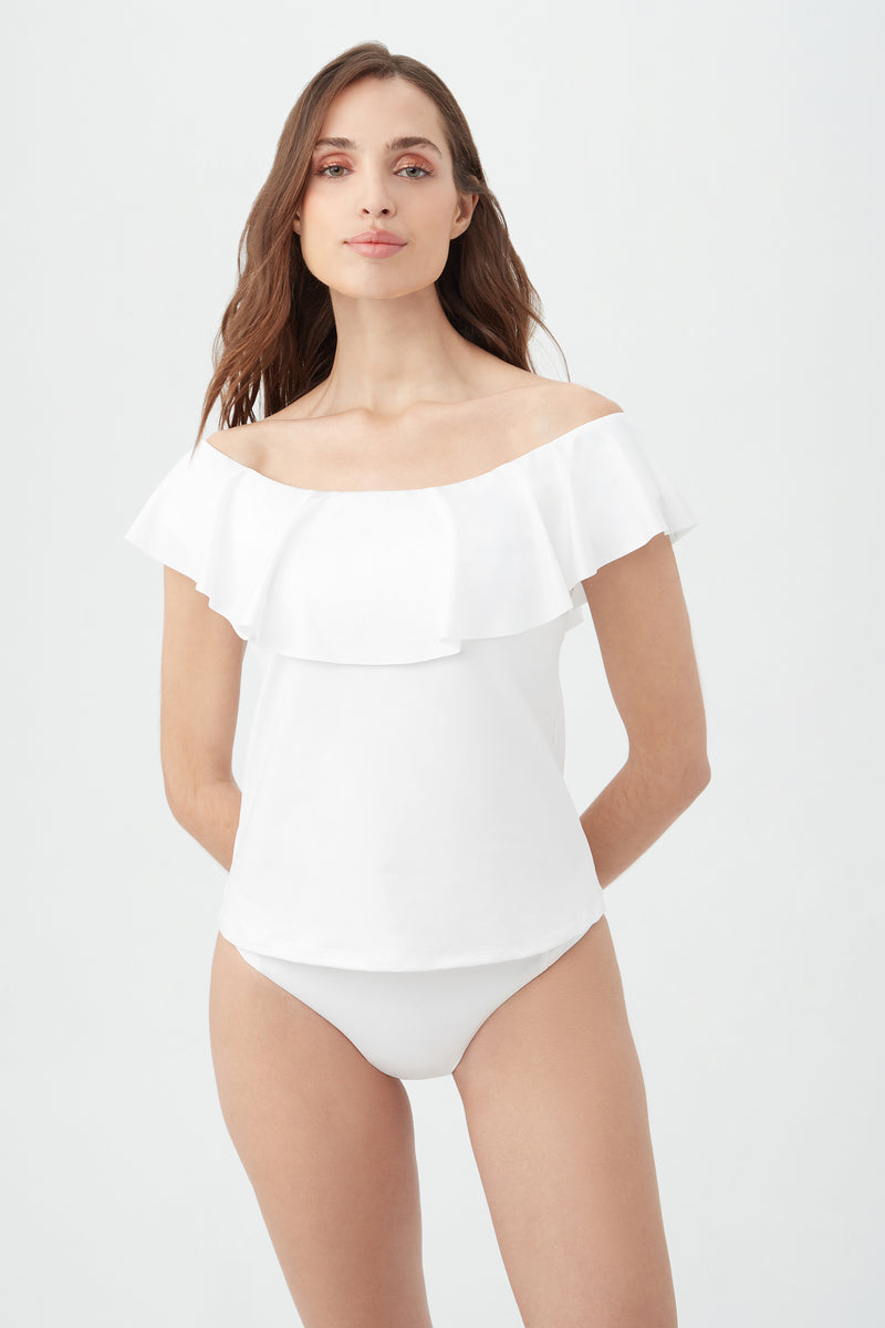 A woman with long brown hair and a relaxed expression wears the Women's Monaco Off The Shoulder Ruffle Tankini Swim Top and matching white bottoms, standing against a plain light background.