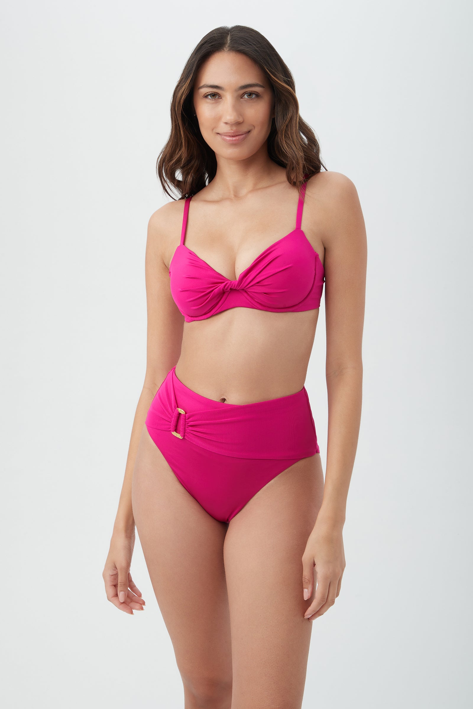 A woman with long wavy hair is smiling at the camera, wearing the Women's Monaco Twist Front Underwire Bra Swim Top in Sangria and a matching high-waisted bottom, standing against a simple light background.