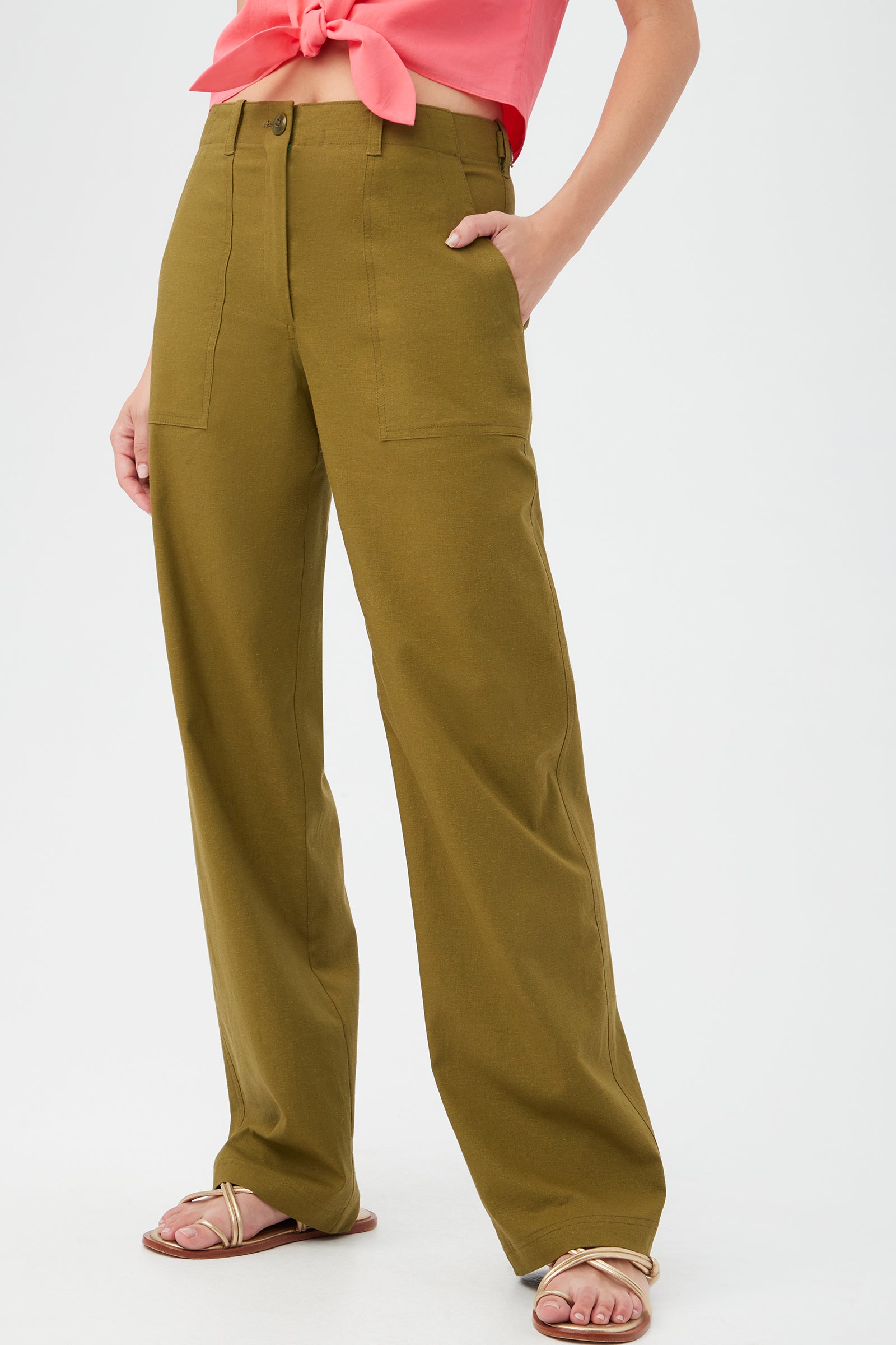 Someone models the Antonia Pant in olive green, featuring a wide-leg cut and front pockets, paired with a coral pink tie-front top and beige sandals. The photo has a plain white background and does not show the model’s head.