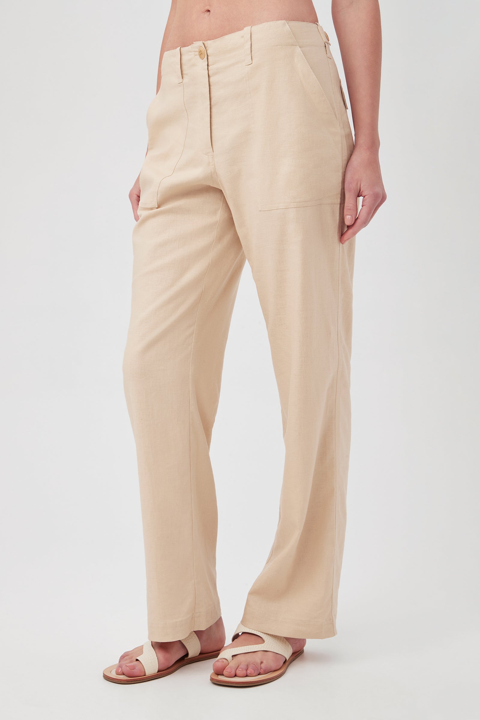 A person models the Antonia Pant—light beige, high-waisted, straight-leg—paired with white sandals. They stand against a plain white background with their hands by their sides and part of their torso visible.