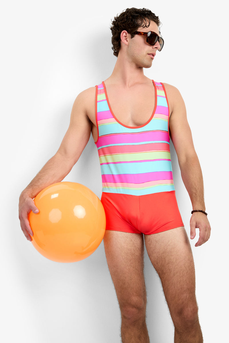 A man in the Sunset Beach Wetsuit - Sol Stripe and sunglasses holds an orange beach ball at his side, looking left against a plain white background.