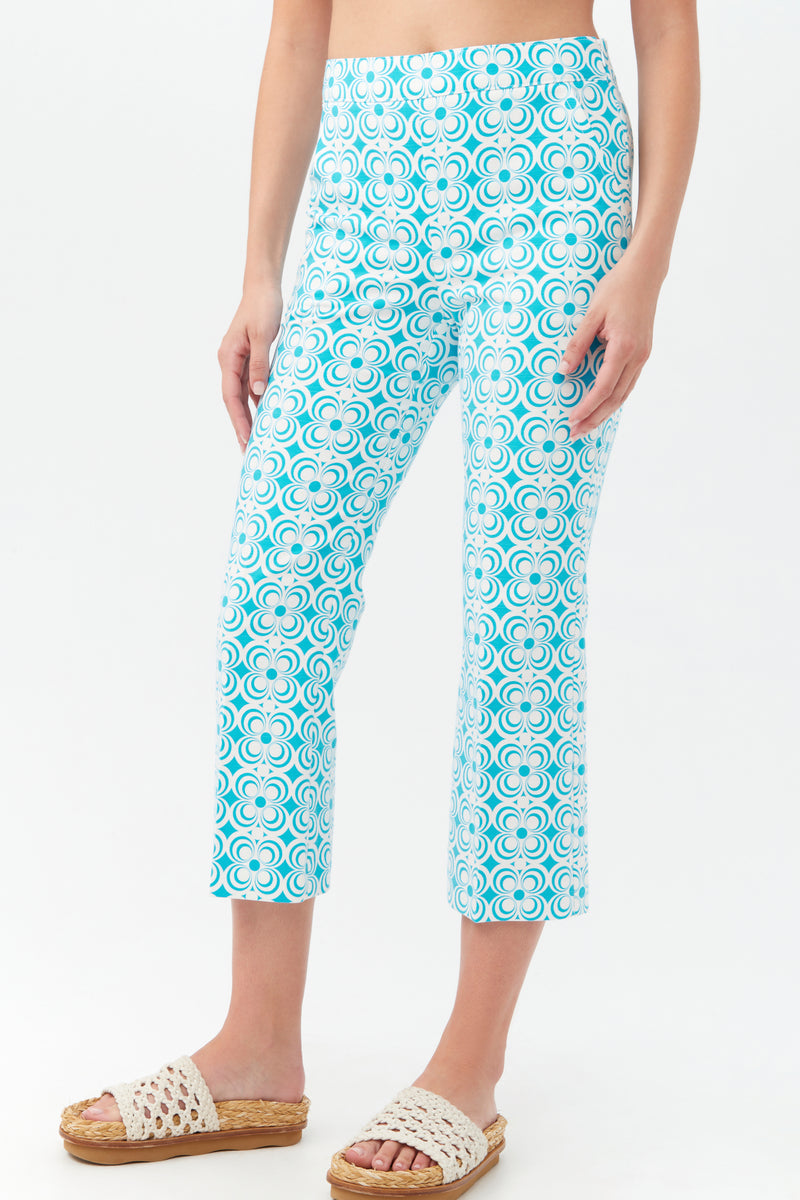 A person wearing Flaire 2 Pant—cropped, blue and white geometric patterned pants—paired with woven slide sandals. The background is plain white.