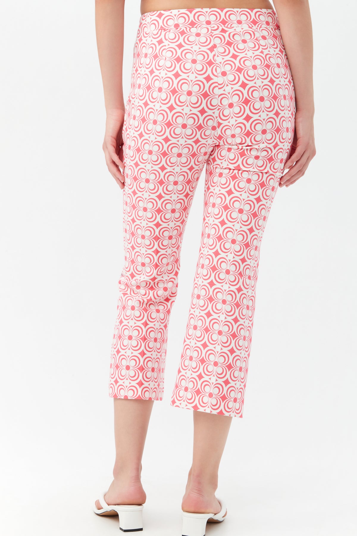 Someone wearing the Flaire 2 Pant, featuring a high-waisted, cropped design with a pink and white retro geometric pattern, stands with their back to the camera. They pair it with white heeled sandals.
