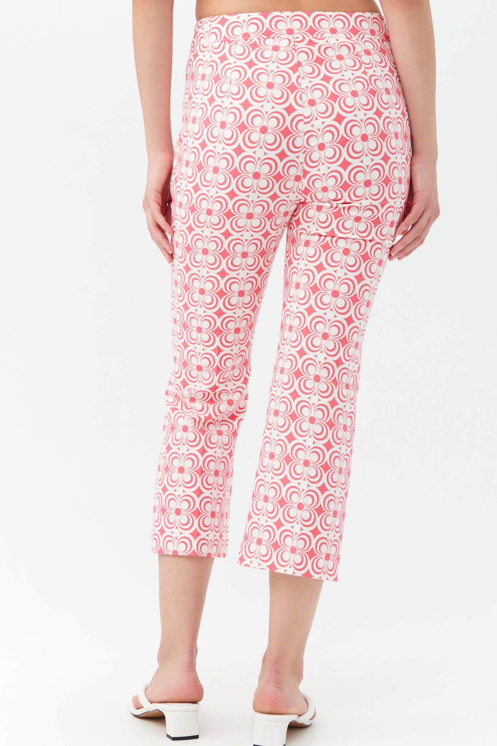 Someone wearing the Flaire 2 Pant, featuring a high-waisted, cropped design with a pink and white retro geometric pattern, stands with their back to the camera. They pair it with white heeled sandals.