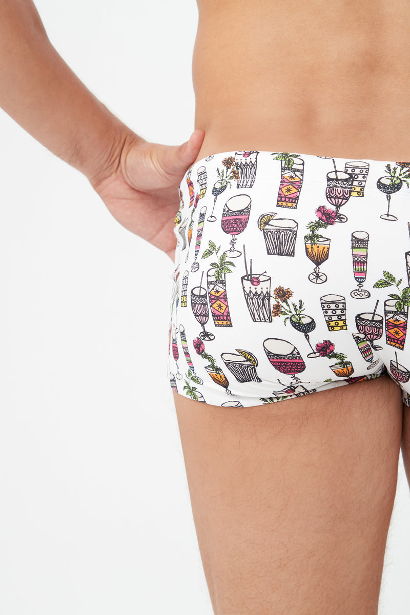 A person wearing the Sorrento Swim Trunk - Happy Hour Swim Knit, featuring colorful cocktail illustrations on white, shown from the side and back against a plain white background.
