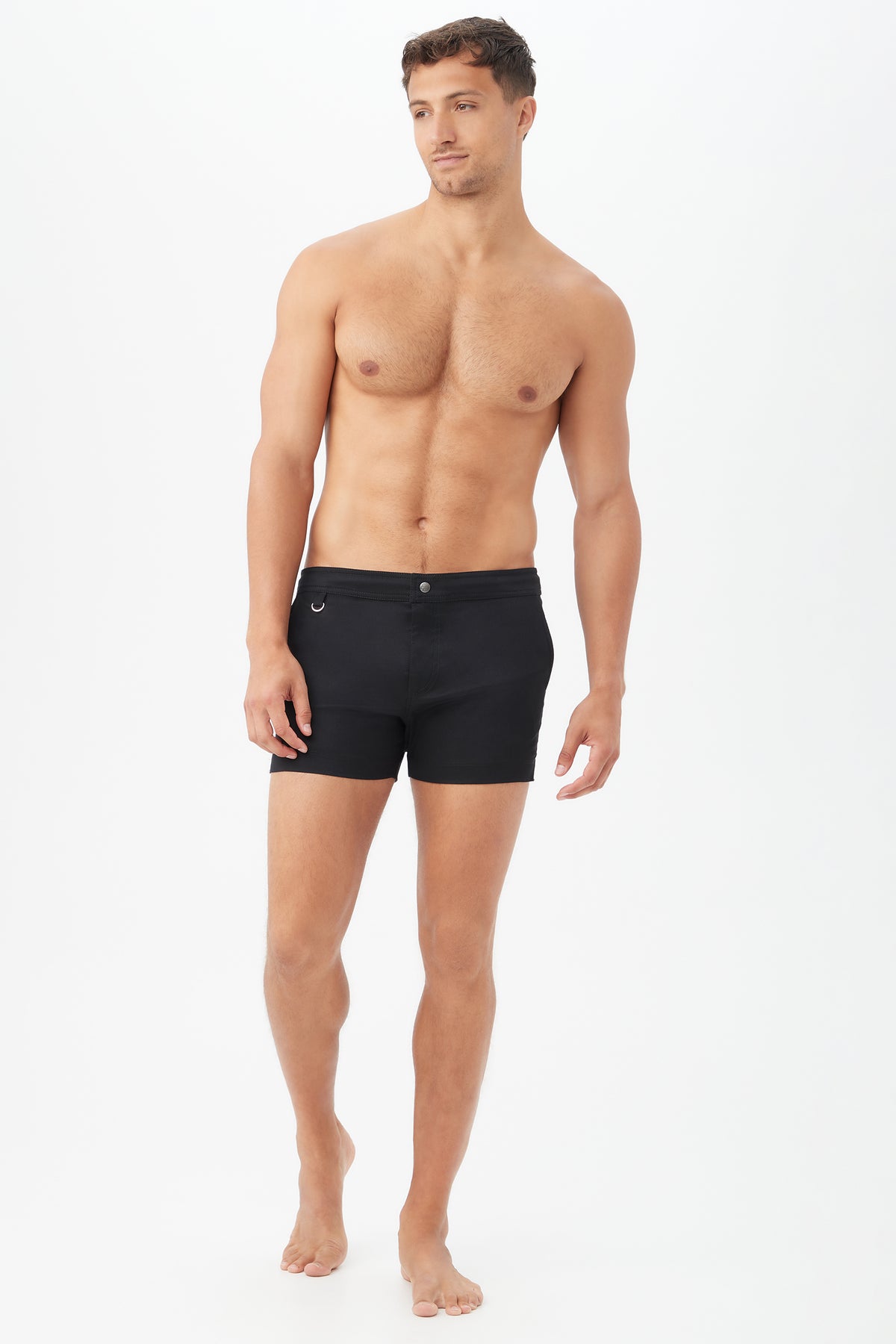 A shirtless man with short hair stands against a plain white background, wearing the Chico Swim Trunk - Metallic Swim Woven in black and no shoes, looking off to the side with a neutral expression.