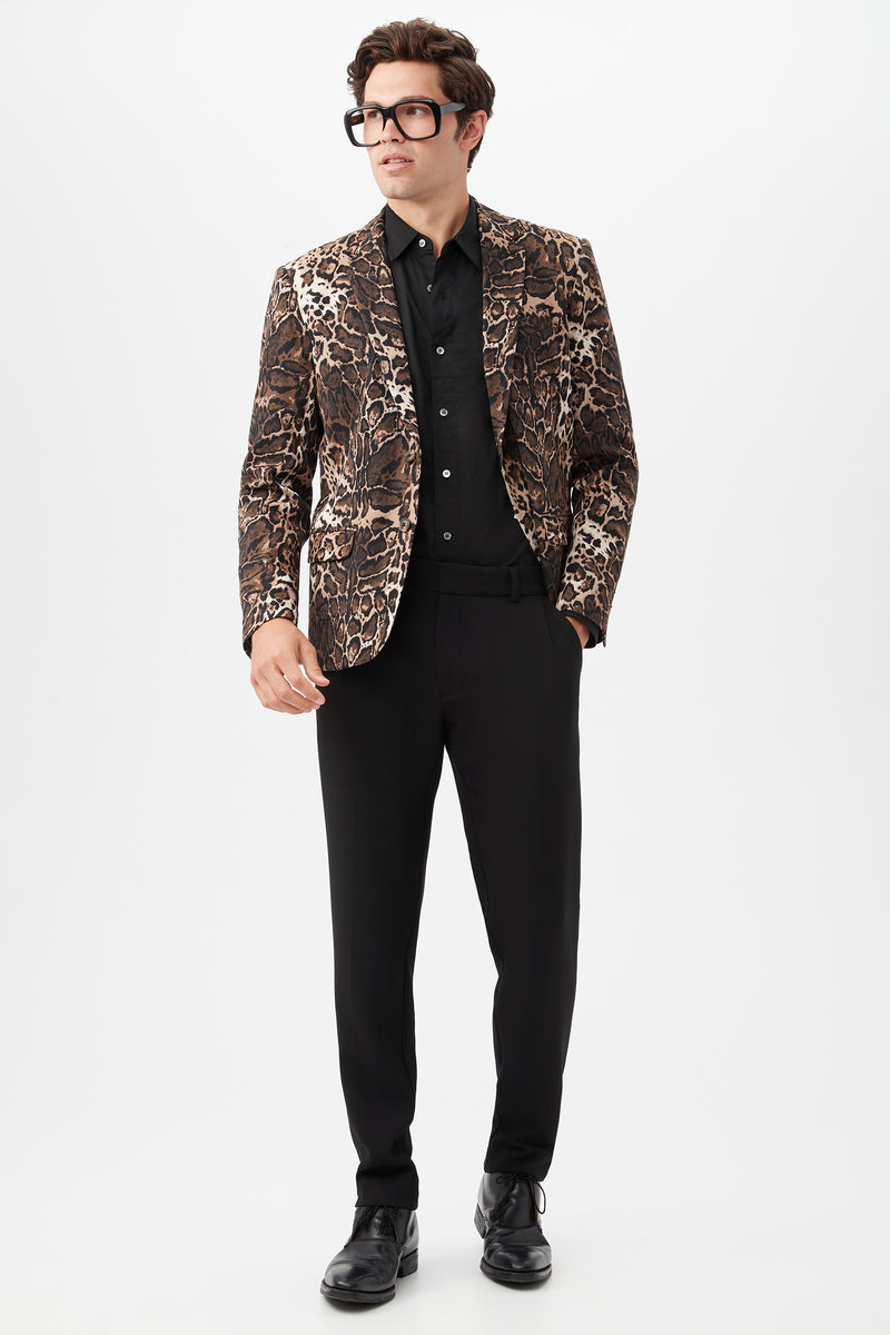 A man stands against a plain white background wearing black glasses, a black shirt, black shoes, a brown leopard-print blazer, and Clyde Slim Trouser - Hi-Line Suiting.