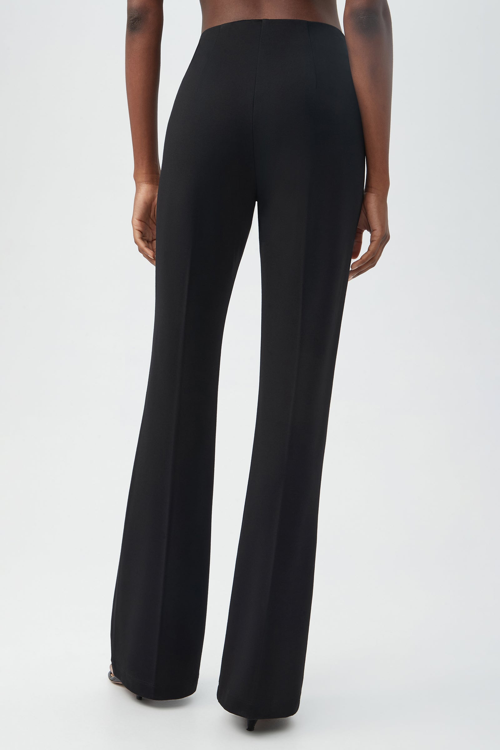 A person is shown from the back wearing Kiara Pant, a pair of high-waisted, black, flared pants, standing against a plain light background.