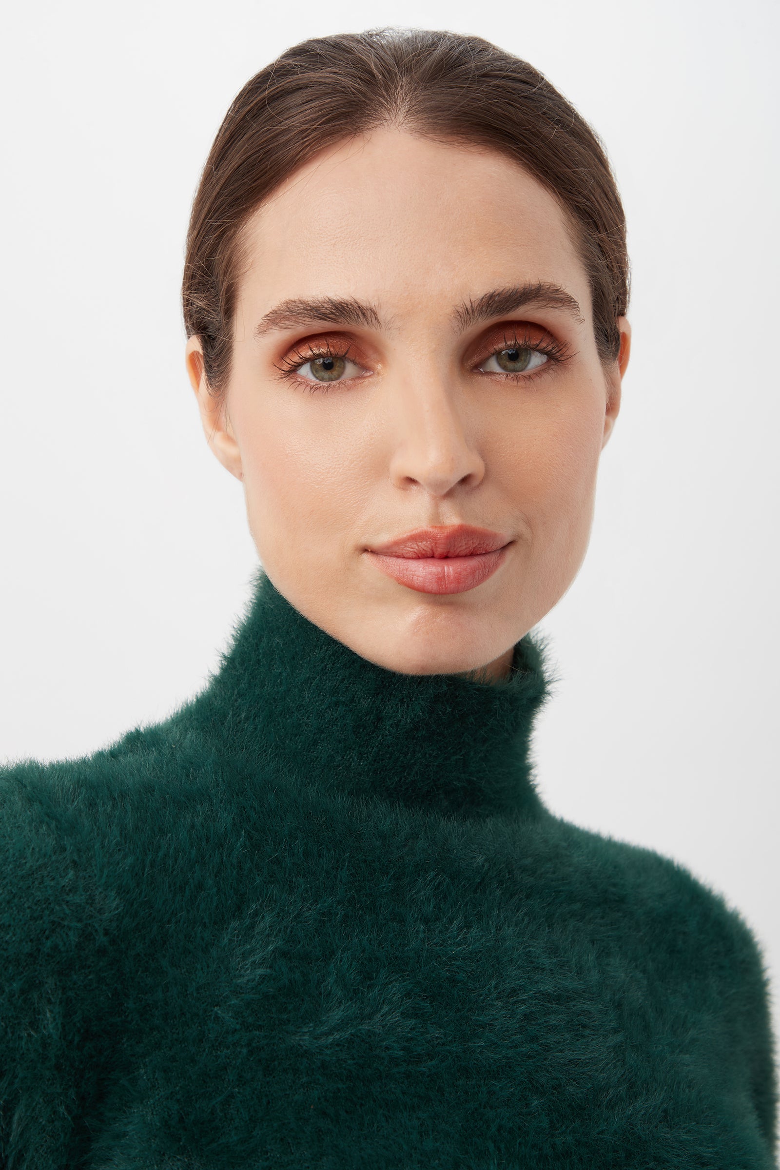 A woman with fair skin and brown hair pulled back wears the Mali Fuzzy Sweater in green, looking directly at the camera against a plain light background.