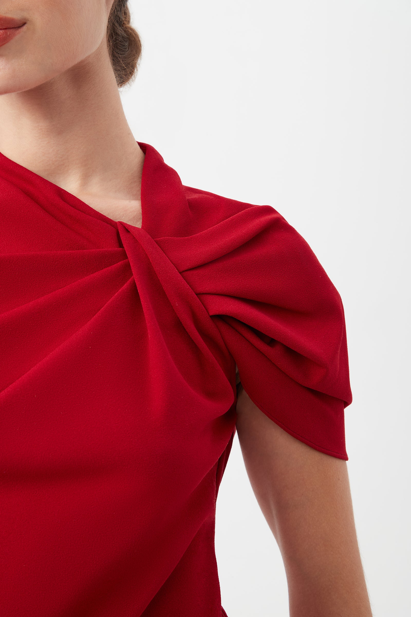 Close-up of a woman wearing the Keshi Asymmetrical Sleeve Top with shoulder twist detail in vibrant red, featuring an asymmetric neckline and elegant draping over one shoulder, set against a plain white background.