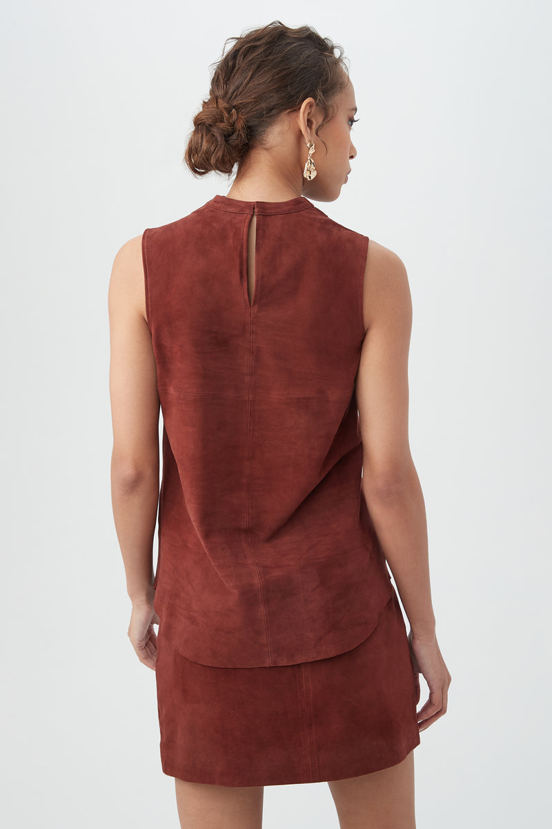 Woman with short curly hair in a low bun, wearing gold earrings and the rust-colored Lenaya 2 Top, shown from the back against a plain light background.