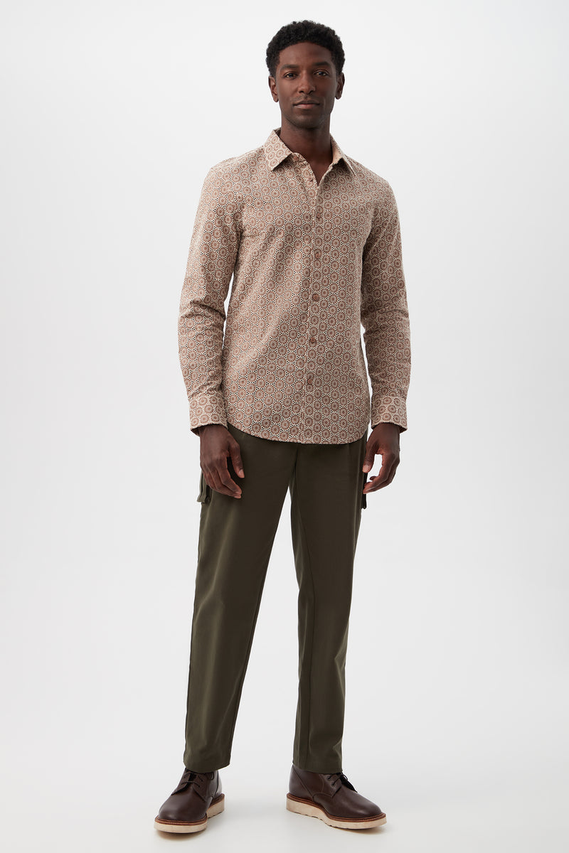 A man stands against a plain background, wearing olive green Lincoln Heights Cargo Trouser - Brushed Twill, a beige patterned button-up shirt, and brown shoes. He faces forward with a neutral expression and relaxed posture.