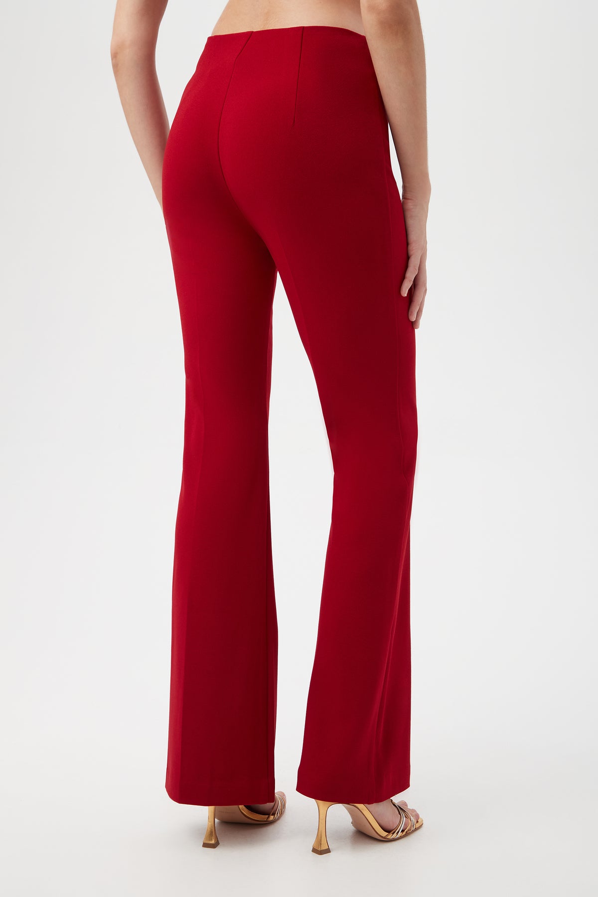 Back view of a woman wearing Jacoba Crepe Knit Tailored Bootcut Pant in red and gold strappy heels against a white background.