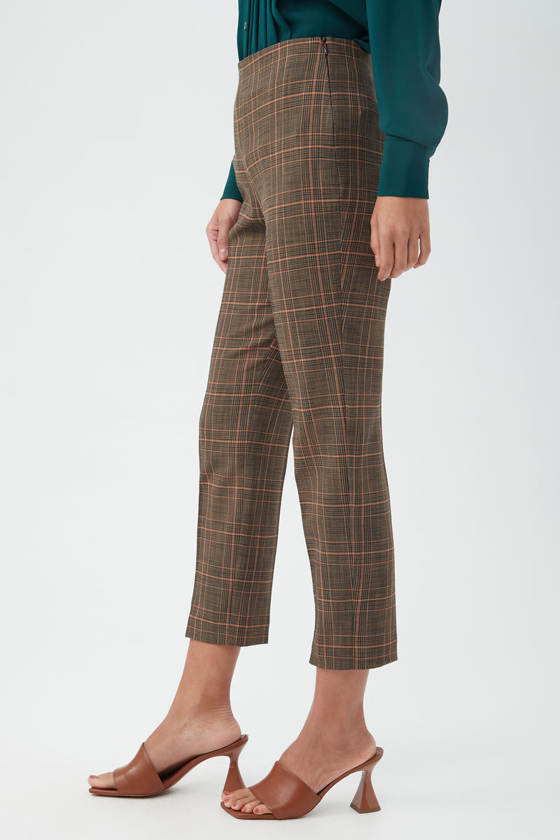 Someone wearing the Masego Pant, a pair of cropped brown plaid trousers, styled with a dark green blouse and brown heeled sandals, stands against a plain light background.