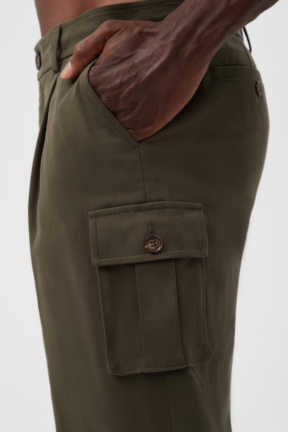 A close-up side view of a person wearing the Lincoln Heights Cargo Trouser - Brushed Twill in olive green, featuring a buttoned flap pocket and their hand in the side pocket against a plain white background.