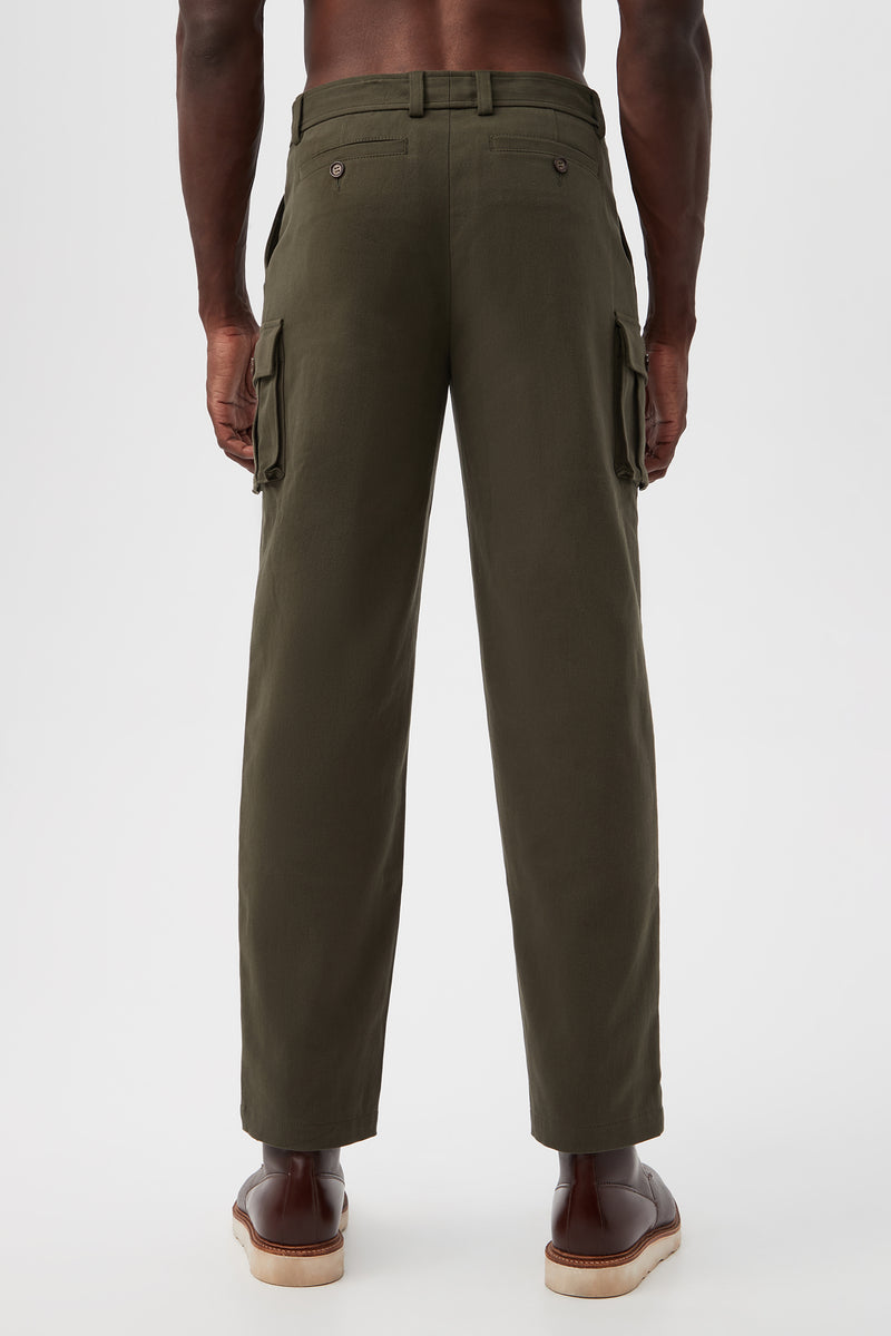 A man stands facing away in Lincoln Heights Cargo Trouser - Brushed Twill in olive green with side pockets and brown dress shoes, set against a plain white background.