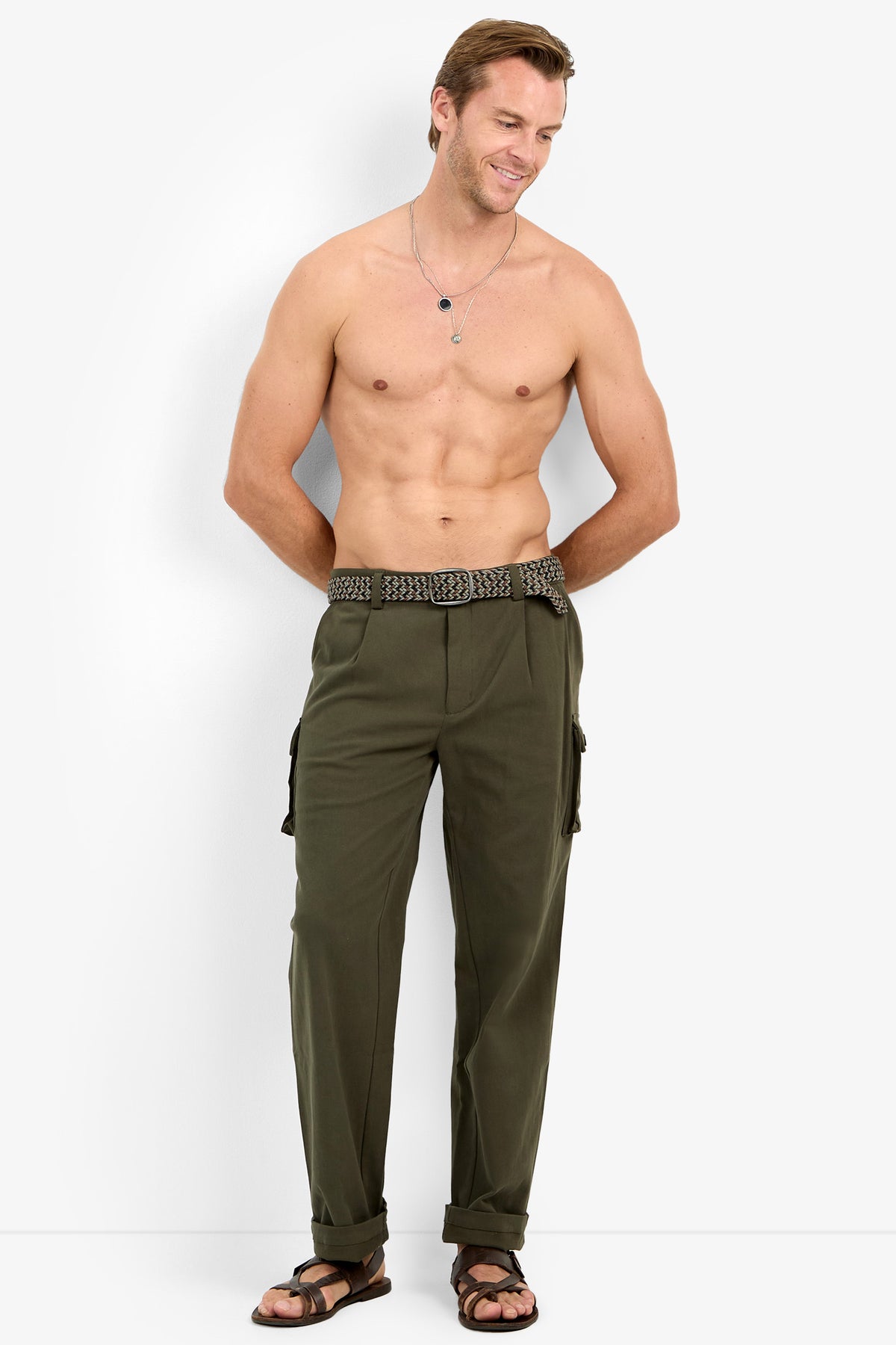 Shirtless man wears the Lincoln Heights Cargo Trouser - Brushed Twill with a woven belt and black sandals, smiling against a plain background.