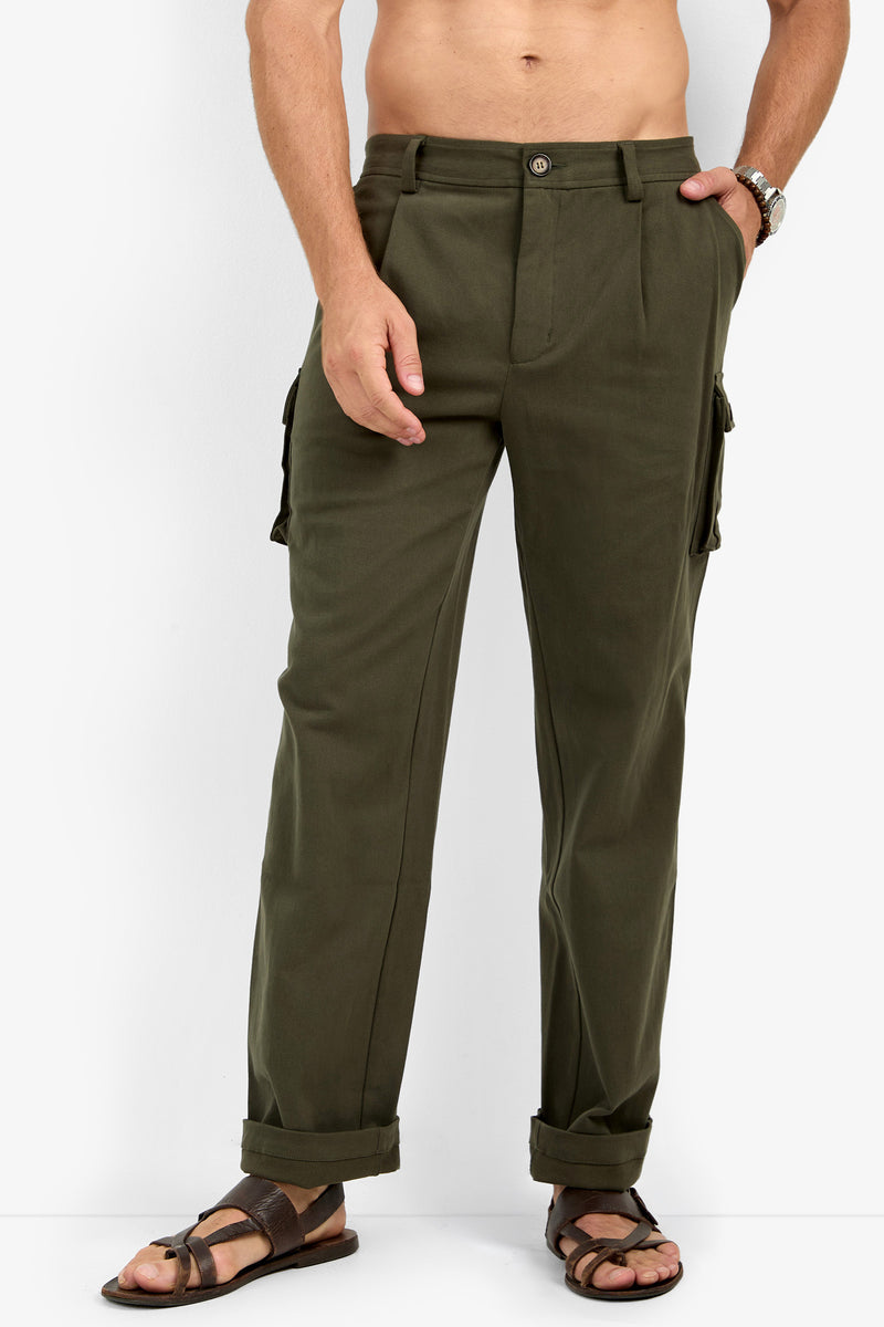 A shirtless person in Lincoln Heights Cargo Trouser - Brushed Twill, olive green with rolled cuffs and brown sandals, stands against a plain white background with one hand in a pocket.