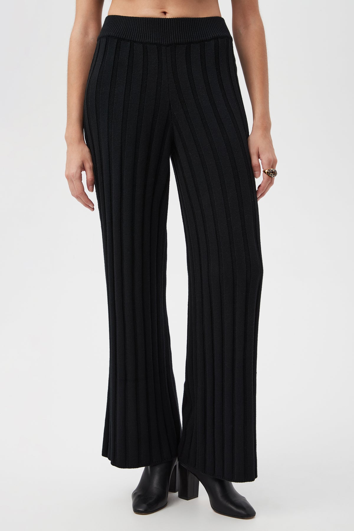 A person models the Pearce 2 Pant in blackâ€”ribbed, wide-leg knit styleâ€”paired with black heeled ankle boots. The waist-down image is set against a plain white background.